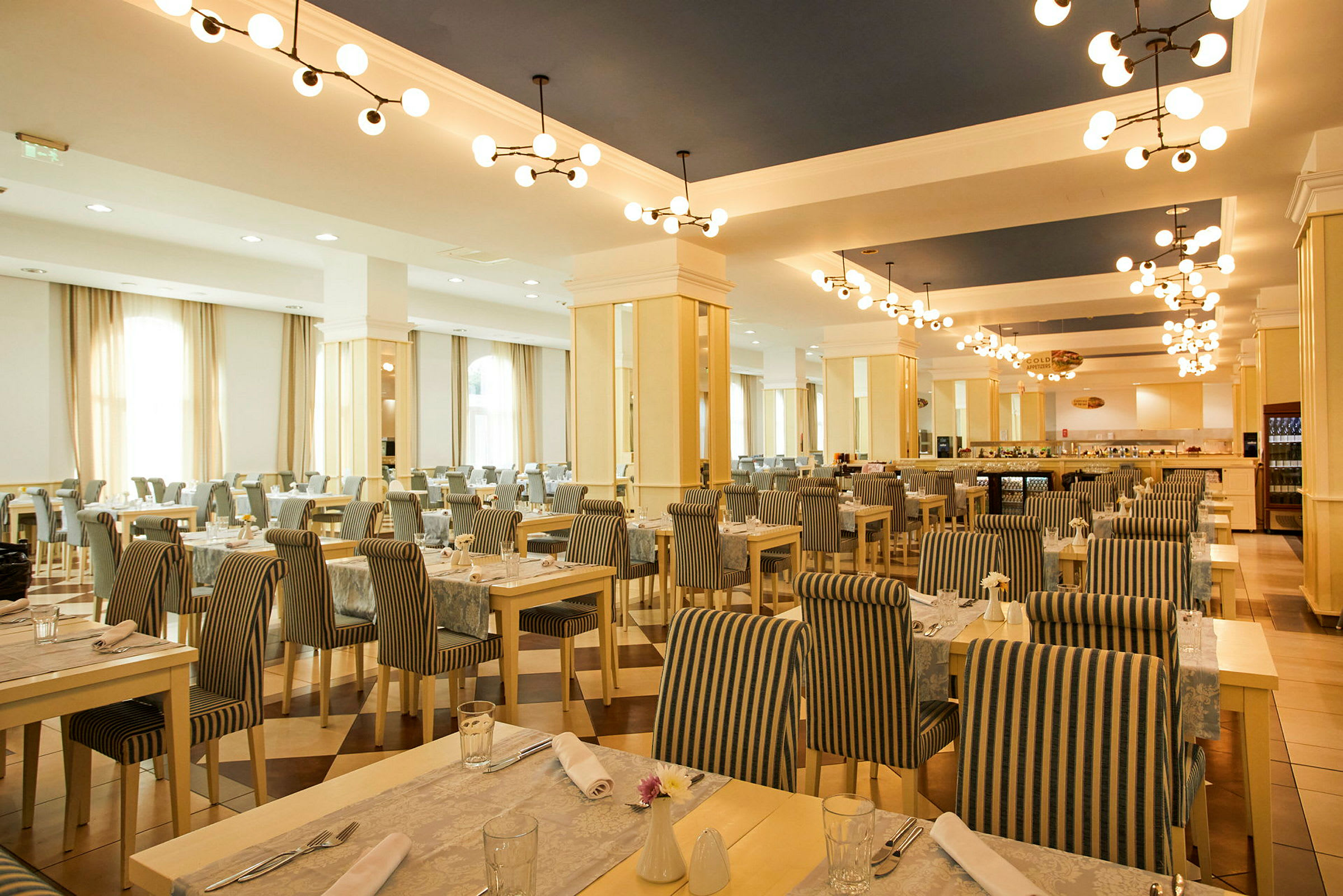 En rymlig restaurang med bord och stolar i randigt tyg och taklampor i modern design. (AI-genererad text)