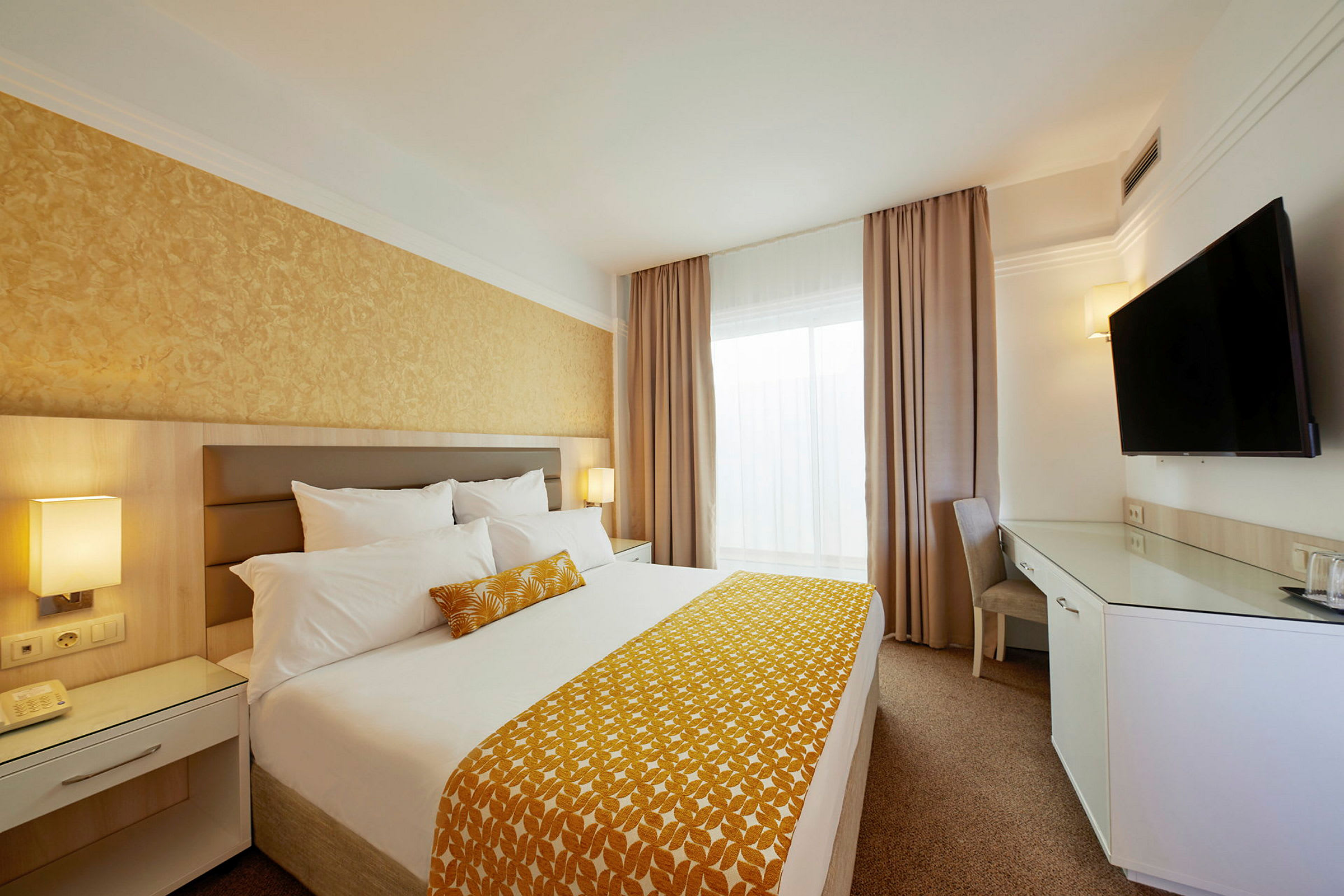 Ett modernt hotellrum med en dubbelsäng, inredning i ljusa toner, en väggmonterad TV och ett skrivbord. (AI-genererad text)