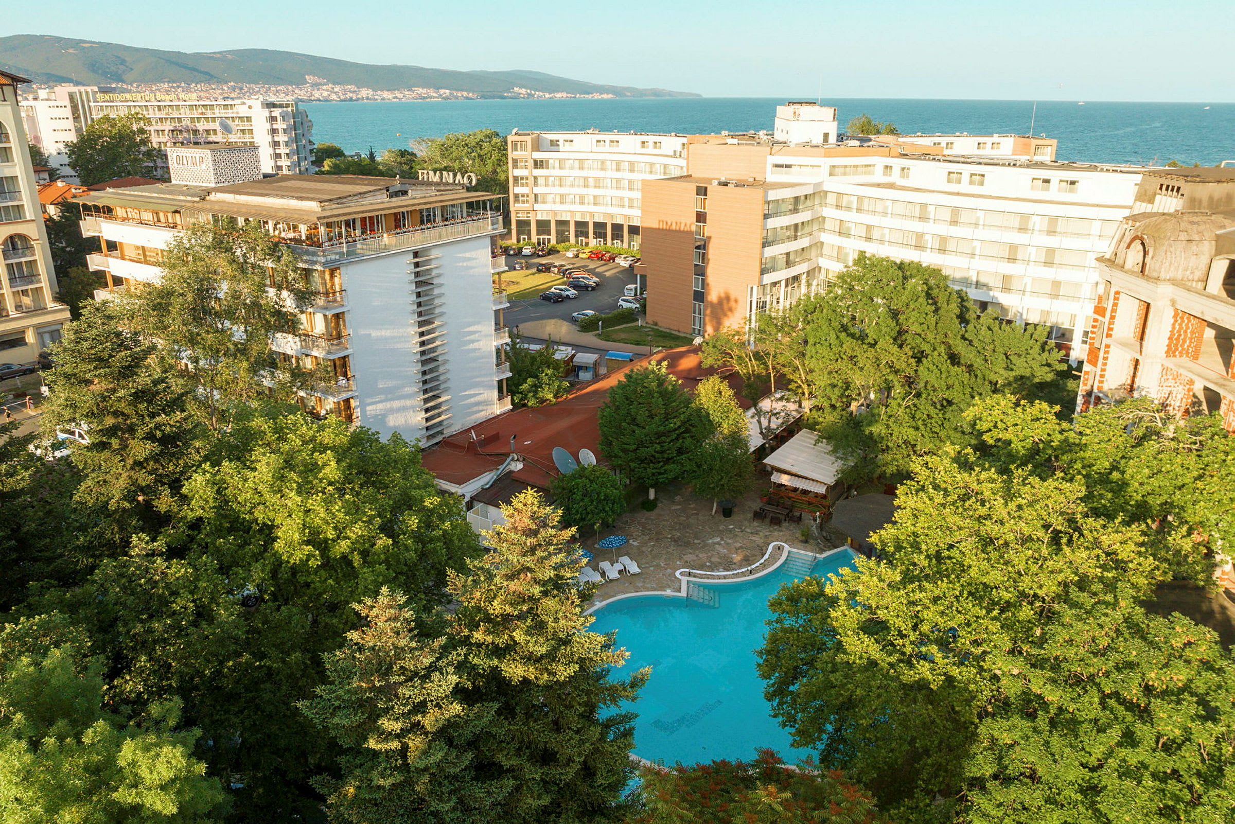 Hotellbyggnader med en pool omgivet av grönska, nära havet. (AI-genererad text)