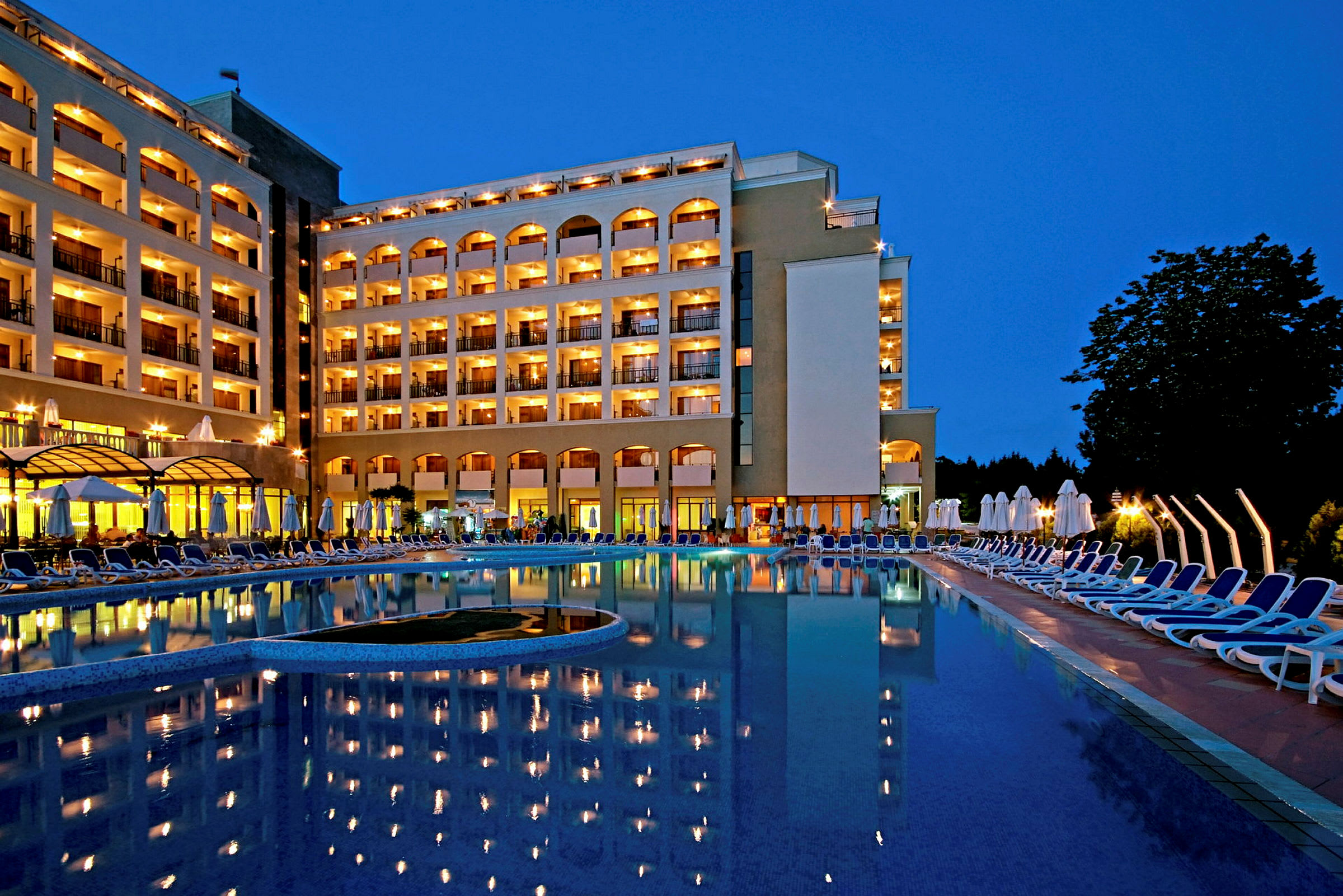 En kvällsbild på en upplyst hotellbyggnad vid en pool som speglar ljusen. (AI-genererad text)