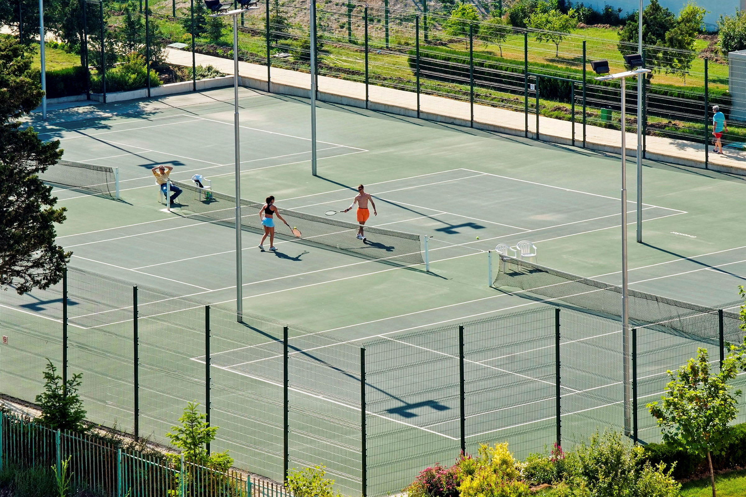 Två personer spelar tennis på en utomhusbana omgiven av grönska. (AI-genererad text)