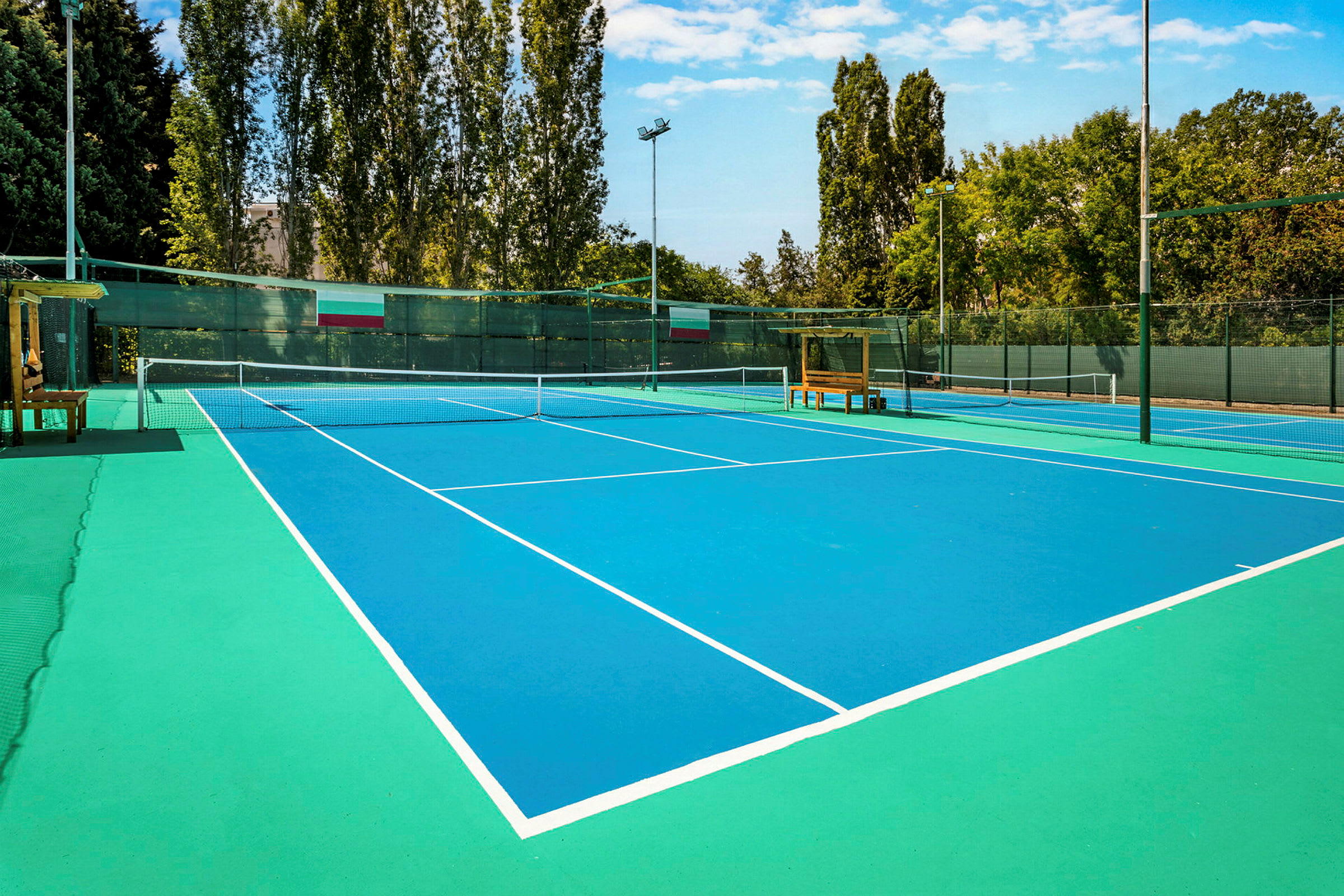 Bild av en tennisbana med blå yta och vita linjer, omgiven av träd och stängsel. (AI-genererad text)