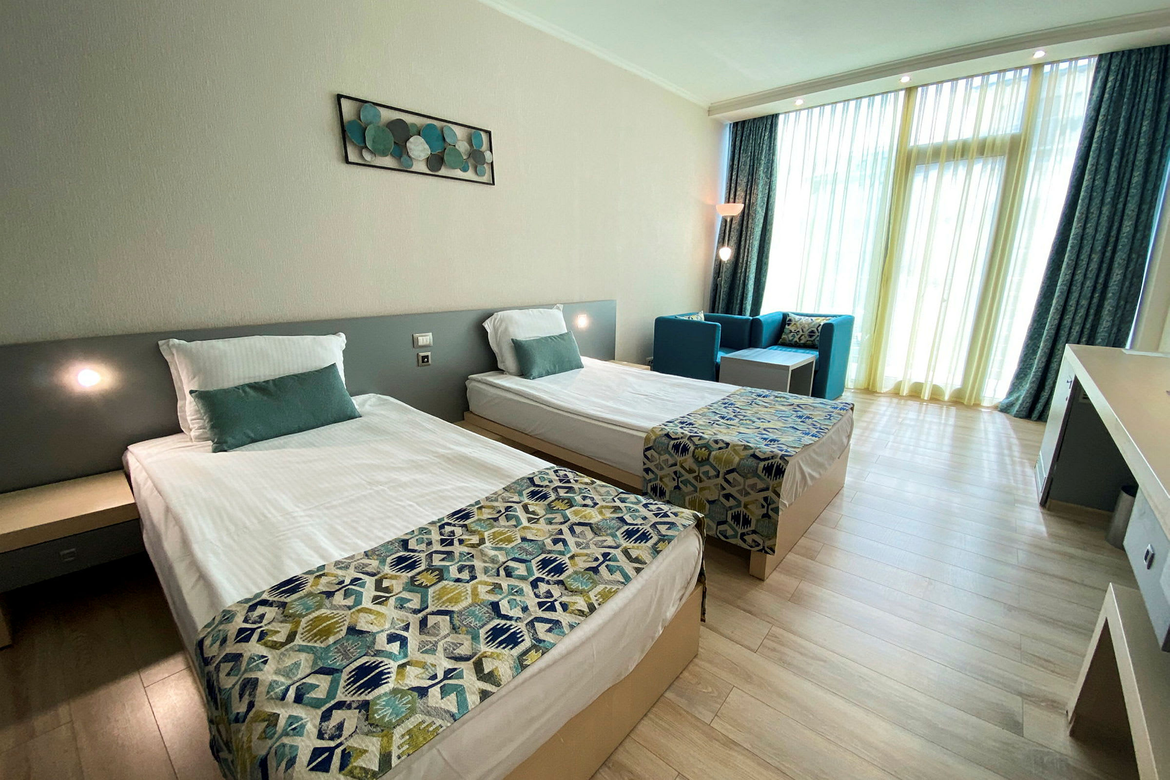 Ett hotellrum med två enkelsängar, en sittgrupp och en stor fönsteryta med gardiner. (AI-genererad text)