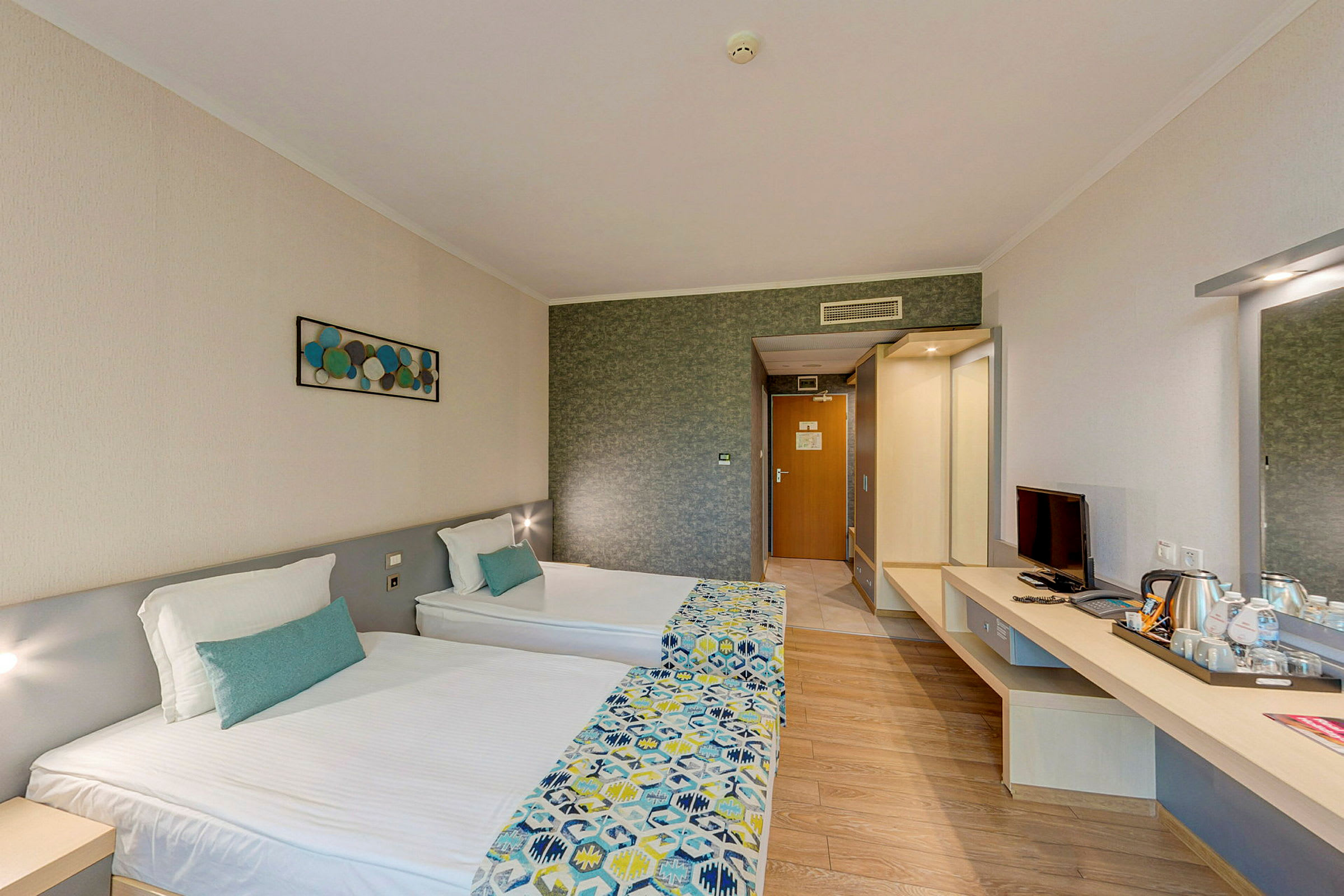 Ett hotellrum med två enkelsängar, en skrivbord med TV och en vattenkokare. Ett konstverk är upphängt på väggen. (AI-genererad text)