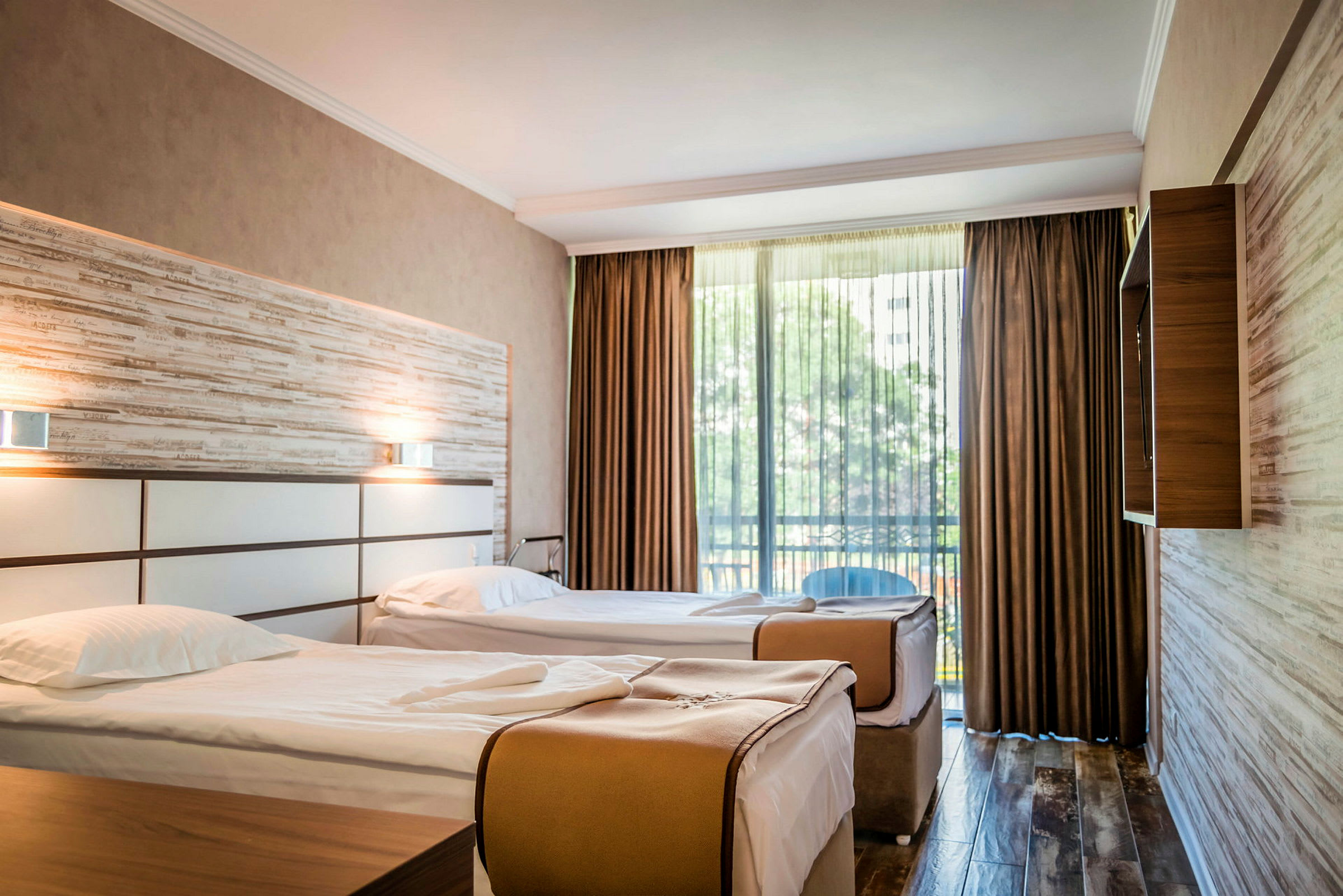 Två enkelsängar i ett hotellrum med stora fönster och gardiner. (AI-genererad text)