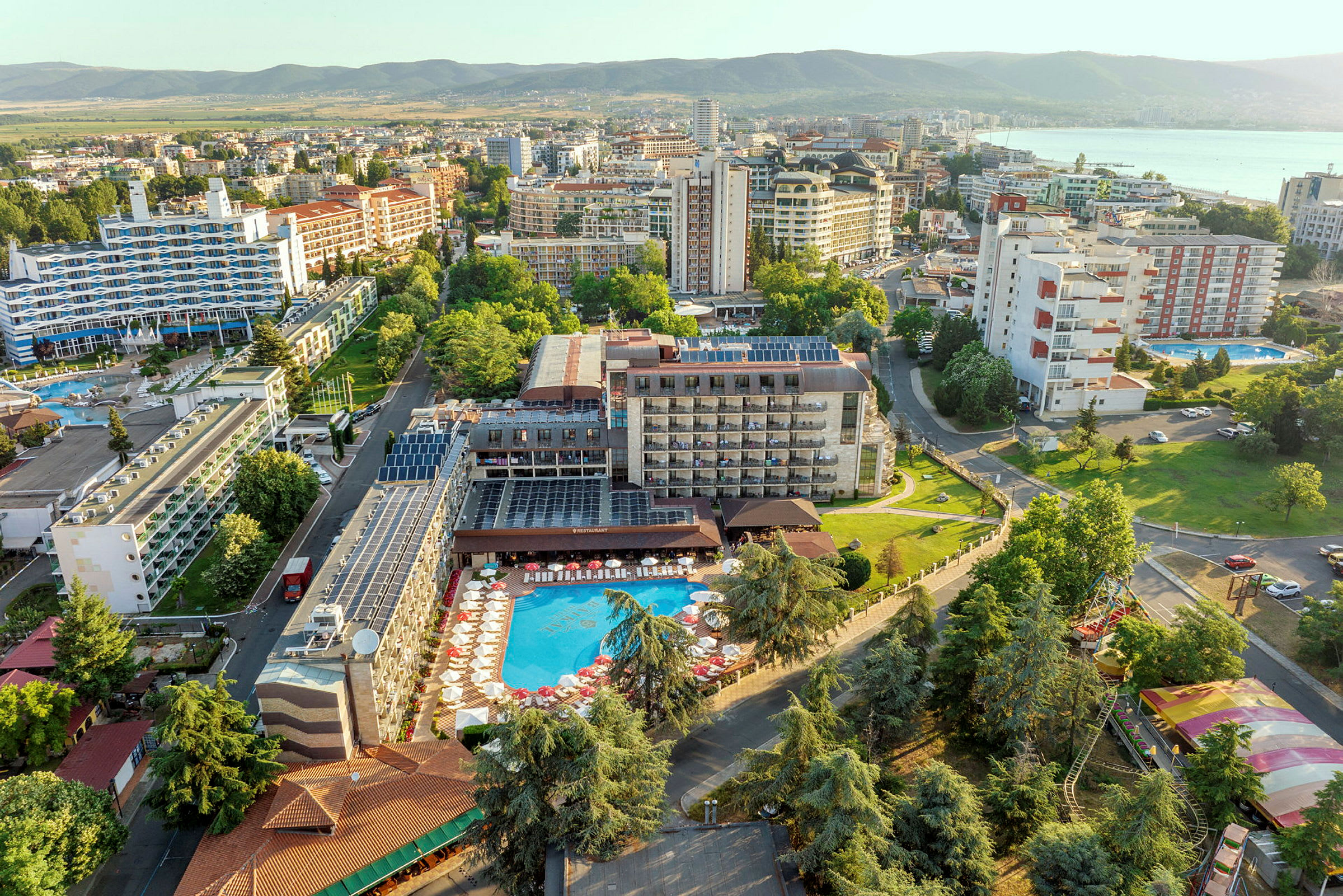 Flygvy av ett hotell med pool och omgivande byggnader i grönskande område. (AI-genererad text)