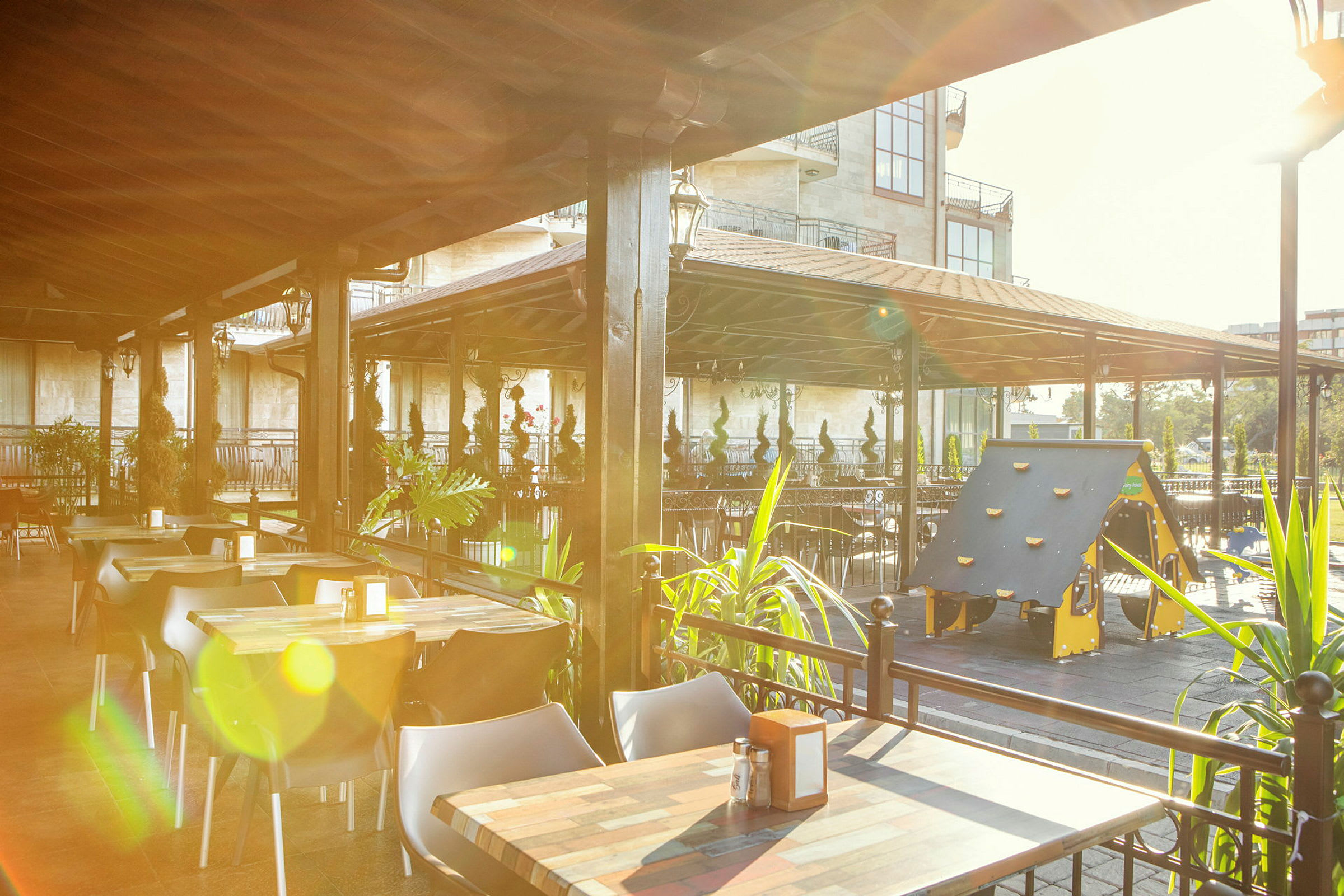 En utomhusrestaurang med bord, stolar och en lekplats för barn under ett tak. (AI-genererad text)