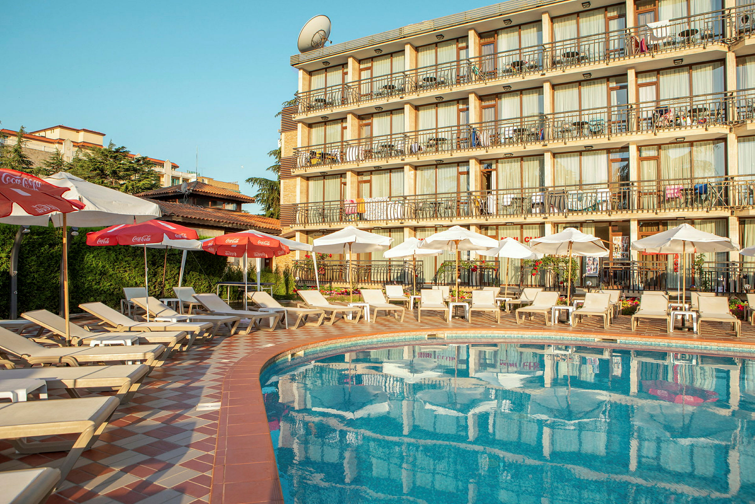 Bild av en hotellpool med solstolar och parasoller, samt hotellbyggnad i bakgrunden. (AI-genererad text)