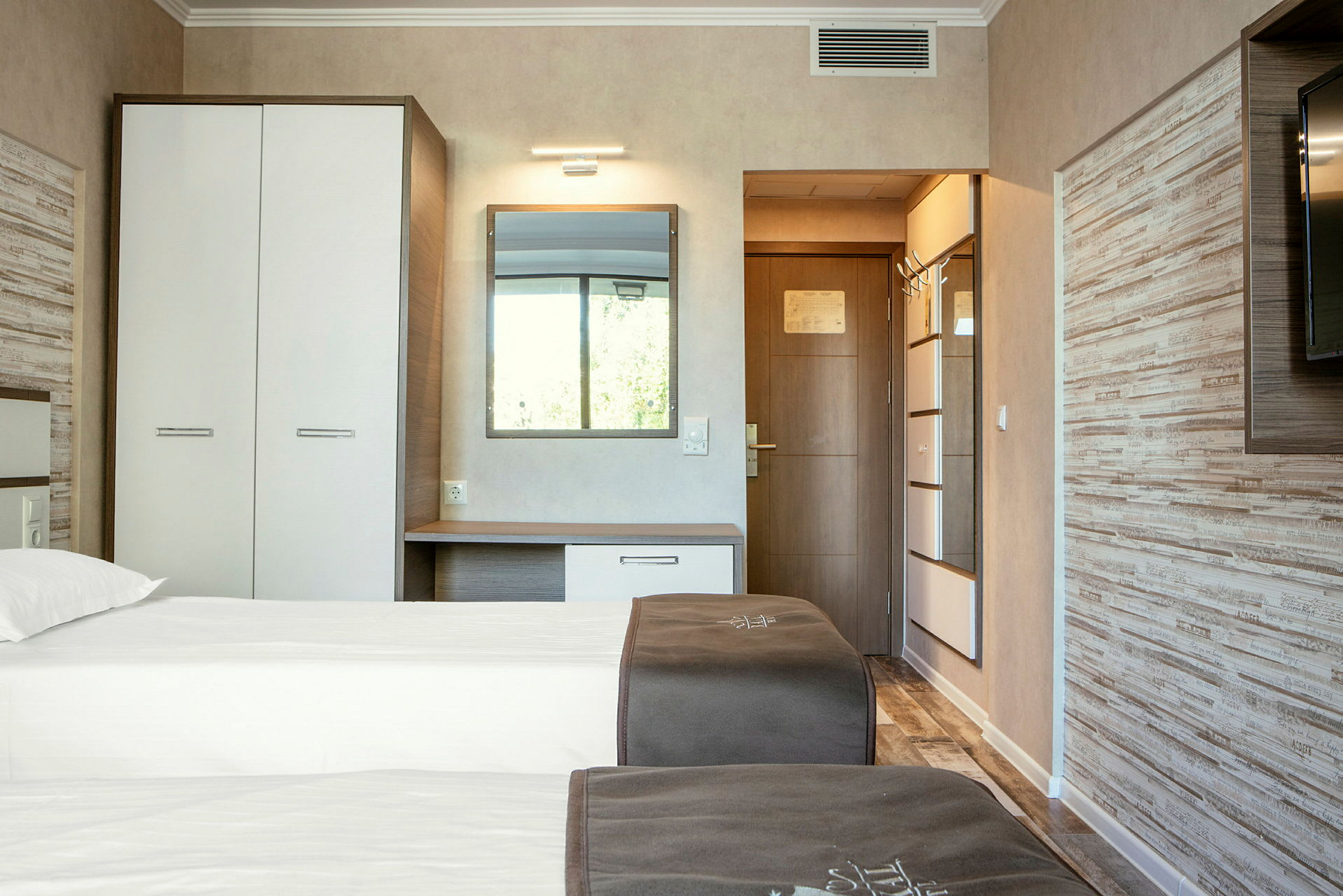 Bild på ett hotellrum med två enkelsängar, garderob, spegel och dörr. (AI-genererad text)