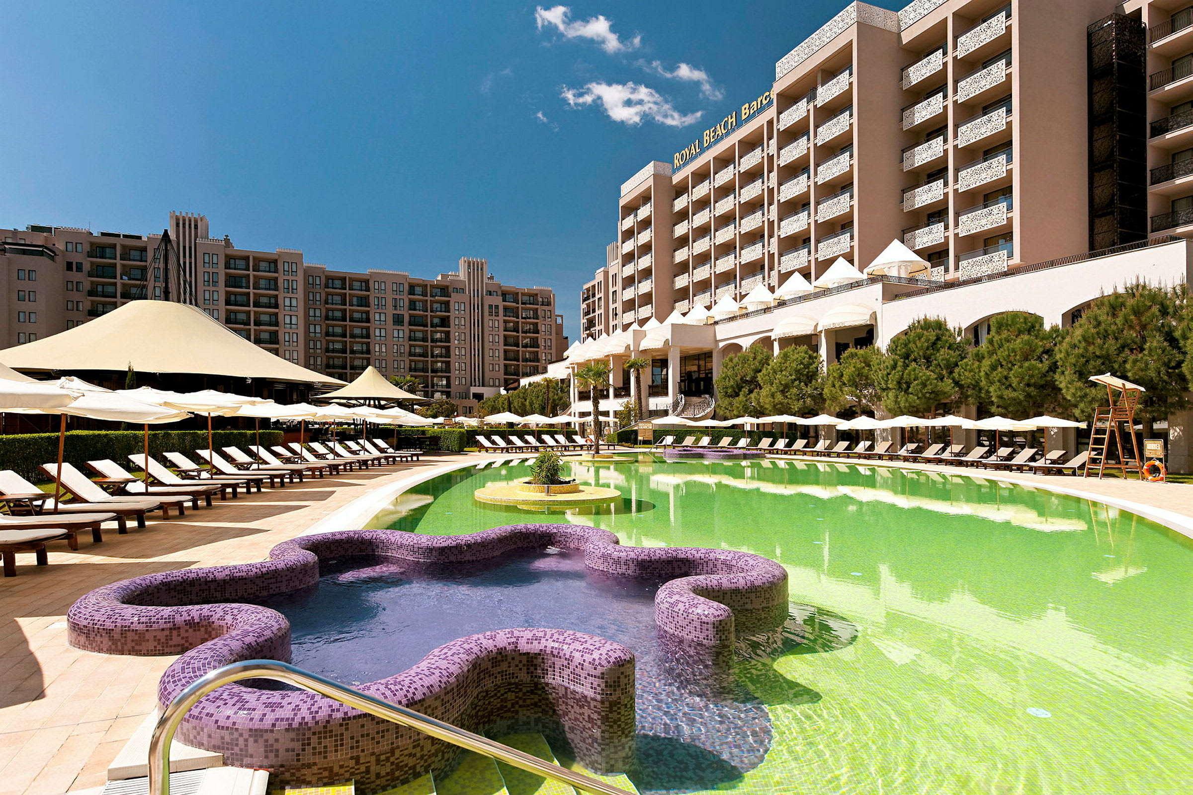 Hotellets utomhusområde med en pool, solstolar och byggnader i bakgrunden. (AI-genererad text)
