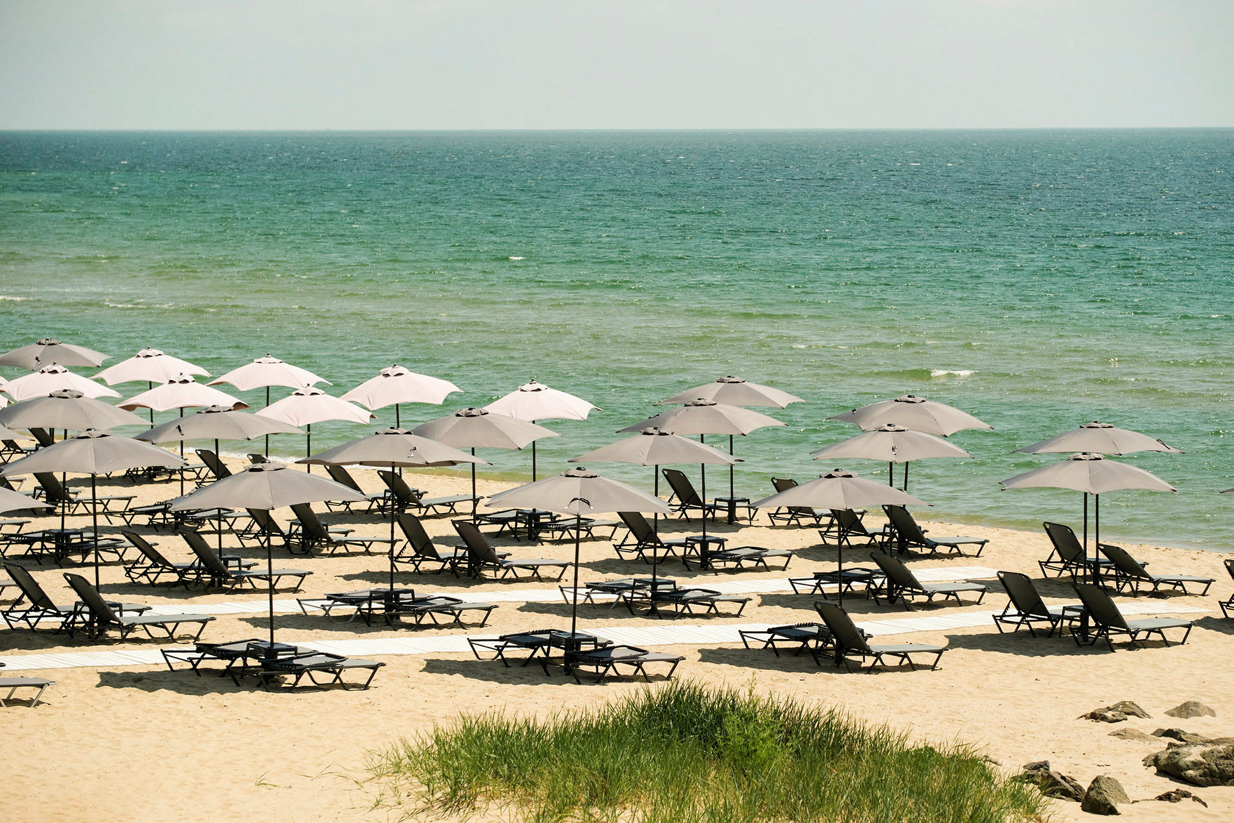 En strand med solstolar och parasoller framför havet. (AI-genererad text)