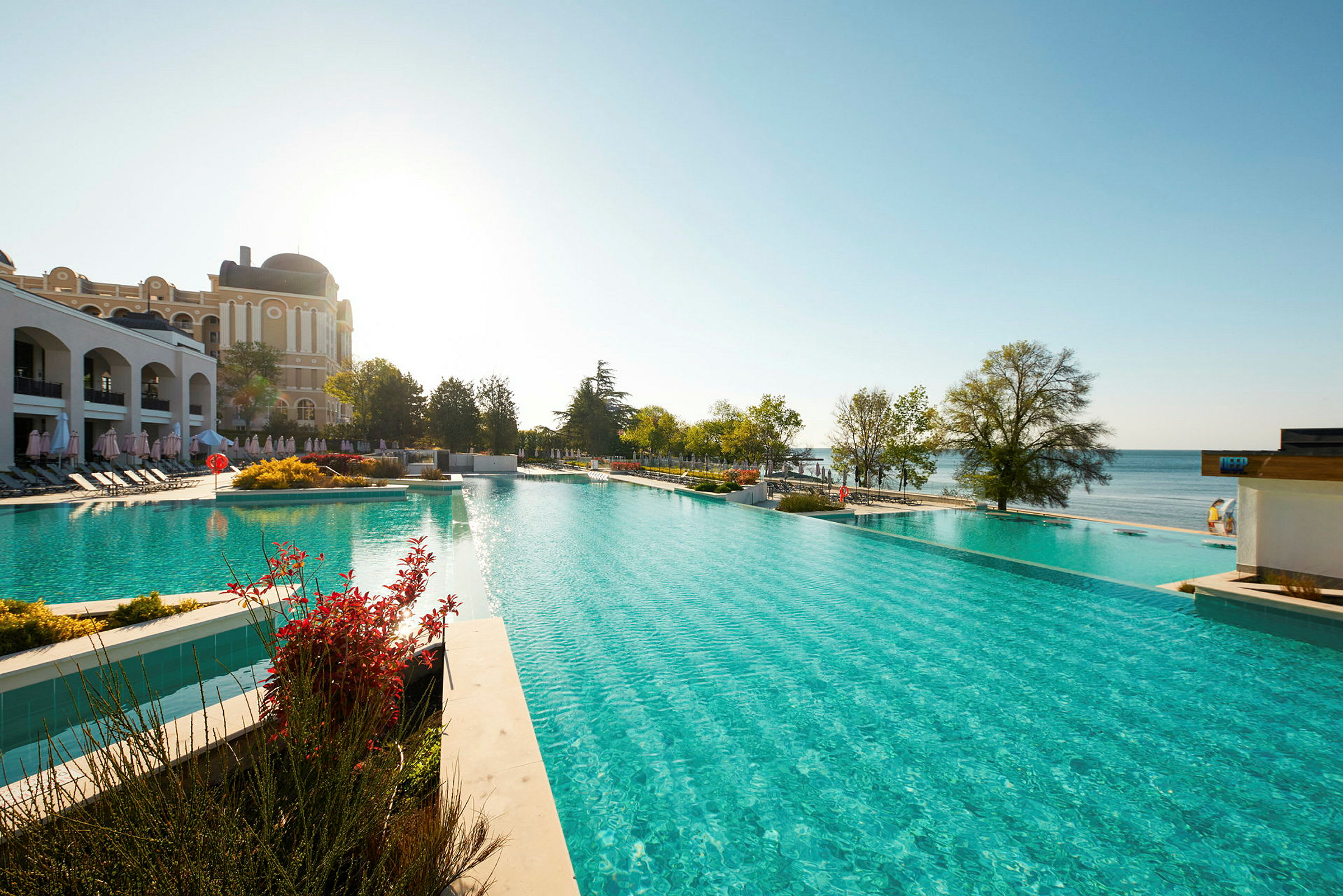 Bild av en stor swimmingpool med en byggnad i bakgrunden och utsikt över havet. (AI-genererad text)