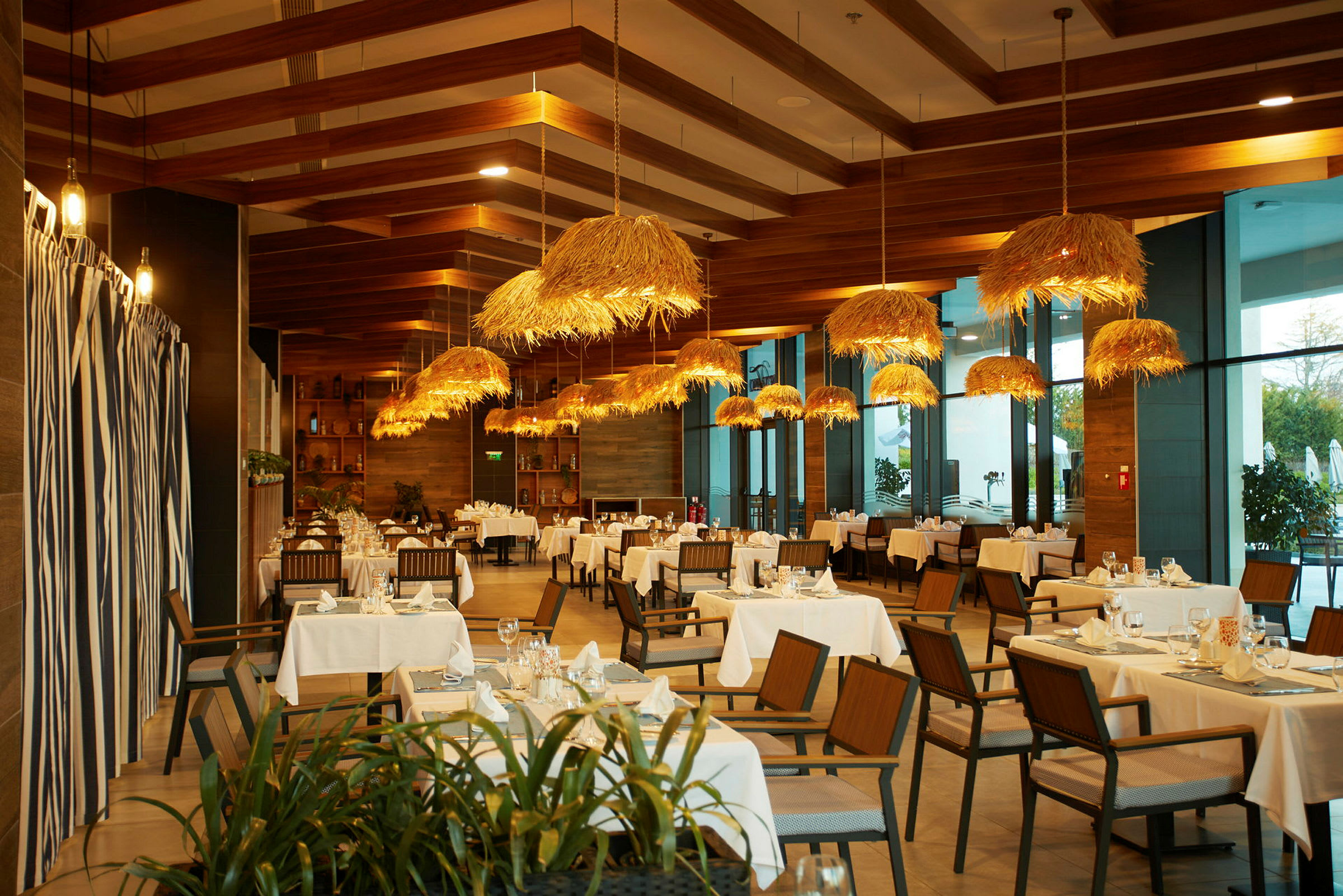 Restaurang med bord, trästolar och hängande lampor med halmdetaljer. (AI-genererad text)