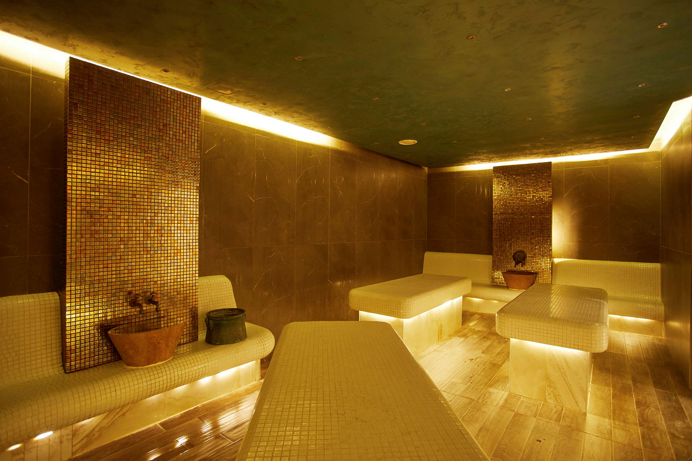 Inomhusbild av ett turkiskt hamam med mosaikväggar och upplysta marmorbänkar. (AI-genererad text)