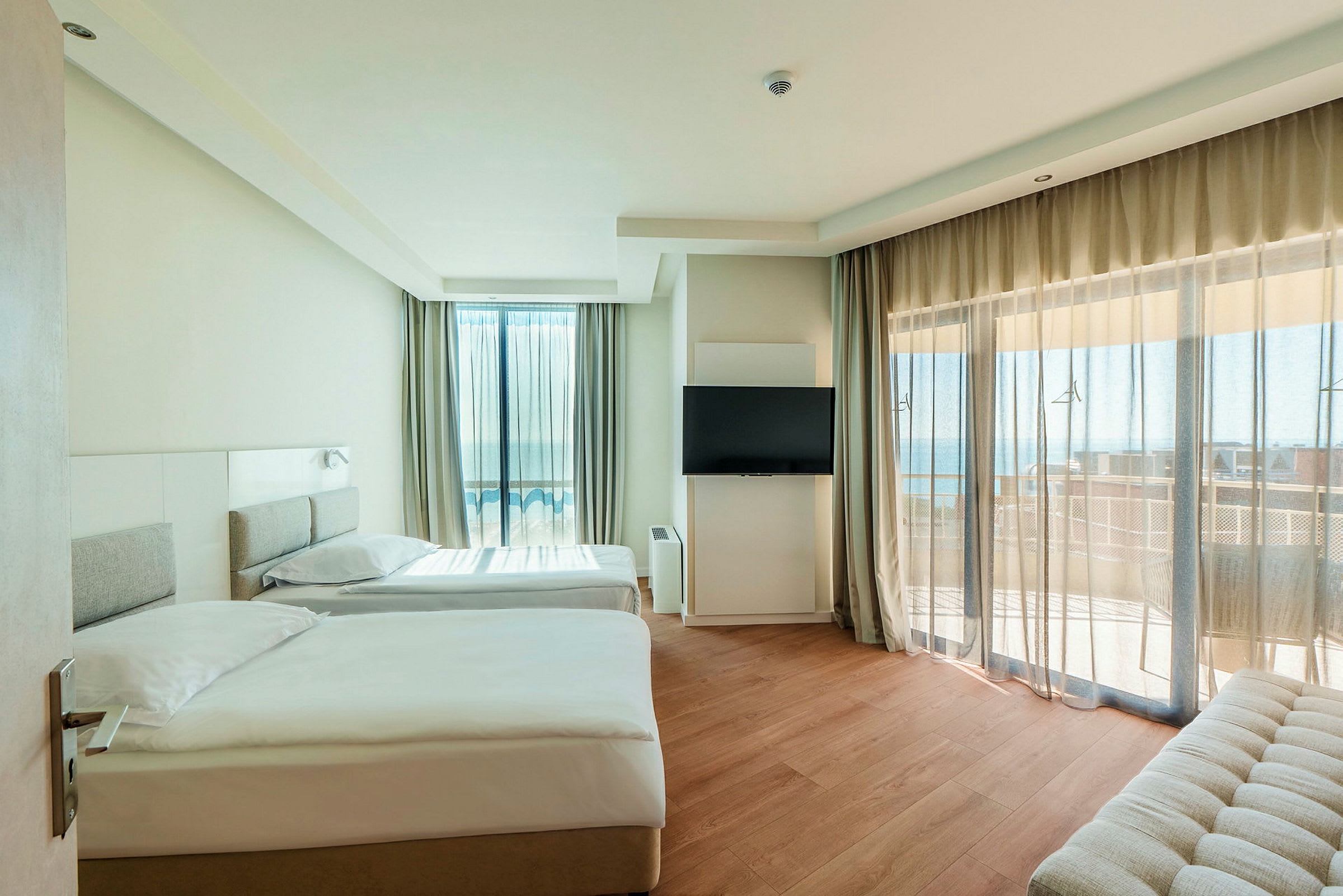 Modernt hotellrum med två enkelsängar, platt-TV och balkong med havsutsikt. (AI-genererad text)