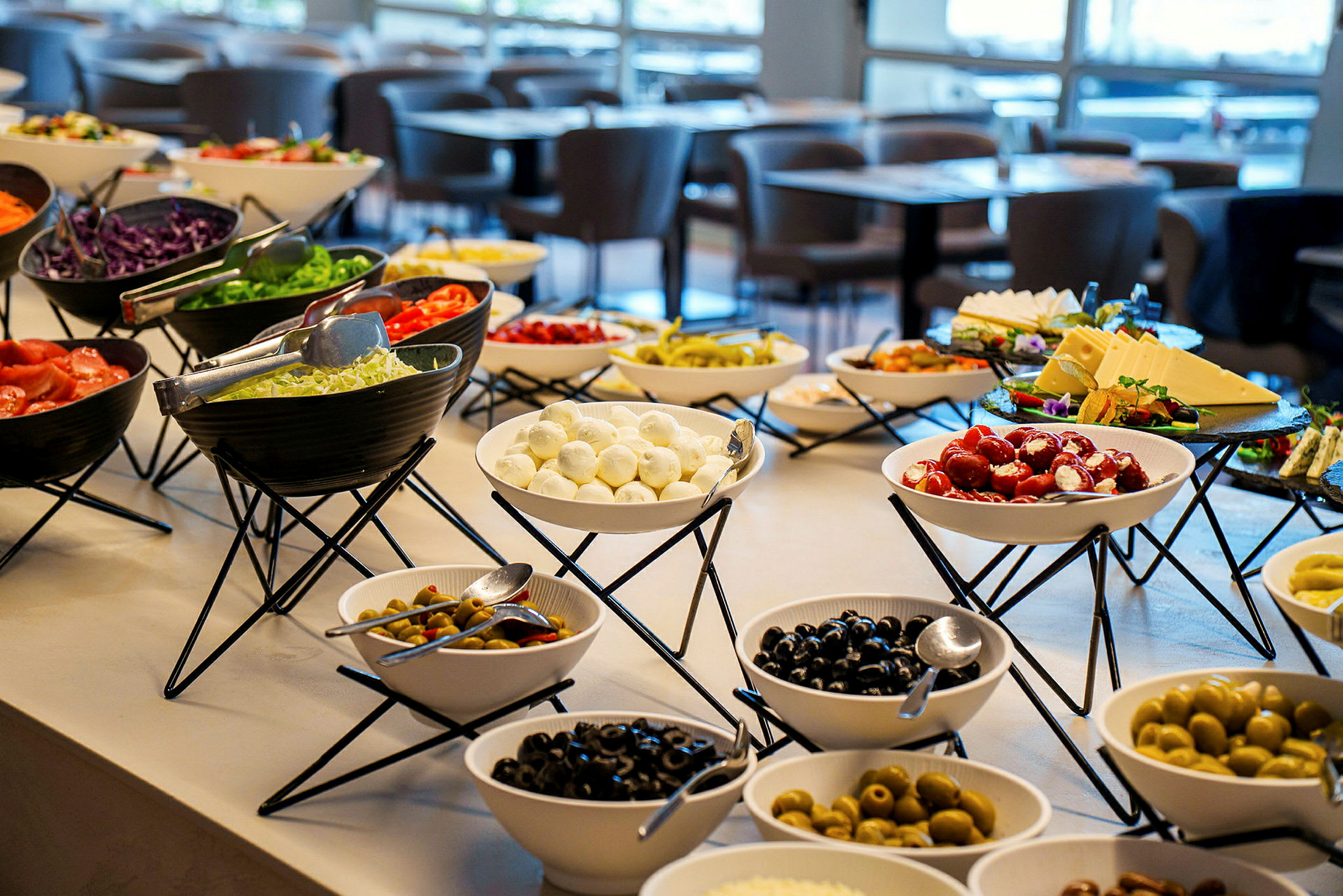 Ett buffébord med olika skålar fyllda med grönsaker, ostar och oliver i en restaurang. (AI-genererad text)