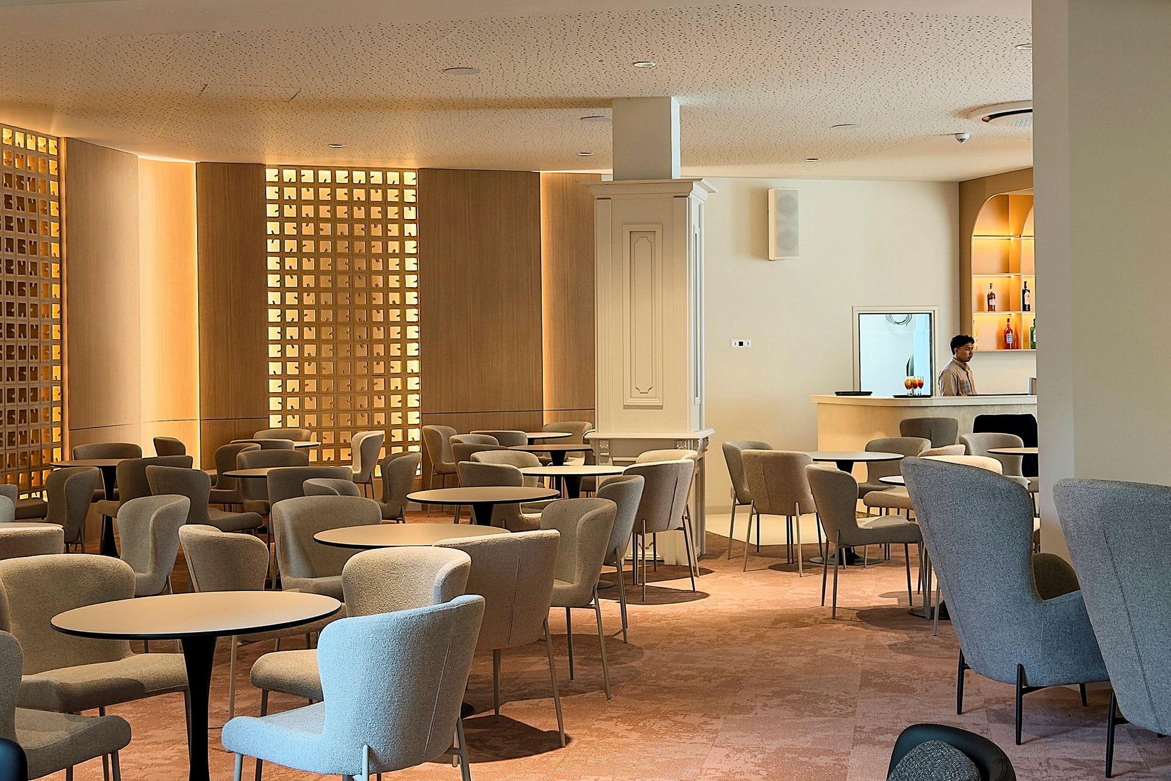 En modern lounge med bekväma fåtöljer och bord. En person står vid en minimal bardisk. (AI-genererad text)