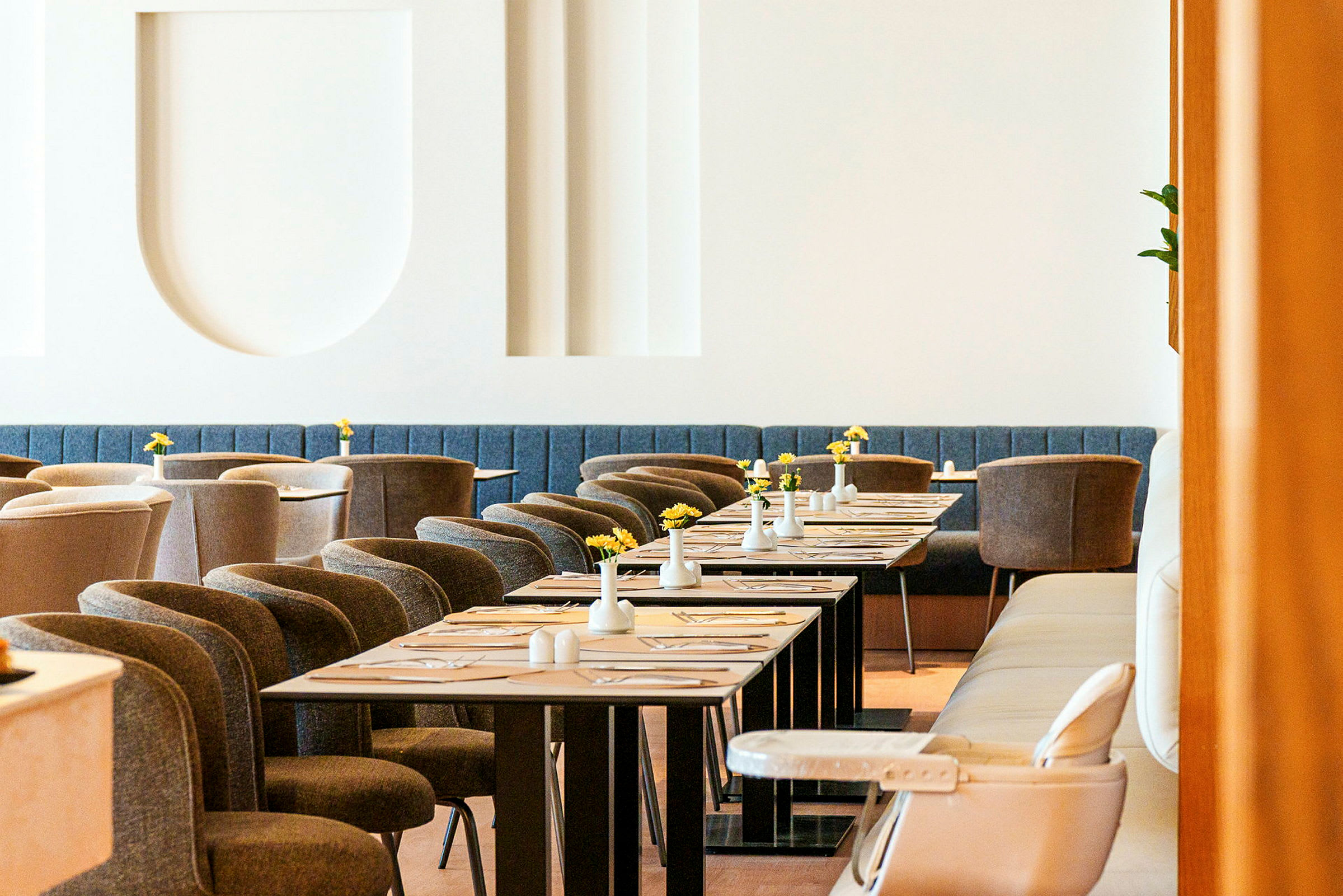 En elegant restaurang med moderna möbler, dukade bord och små vaser med gula blommor. (AI-genererad text)