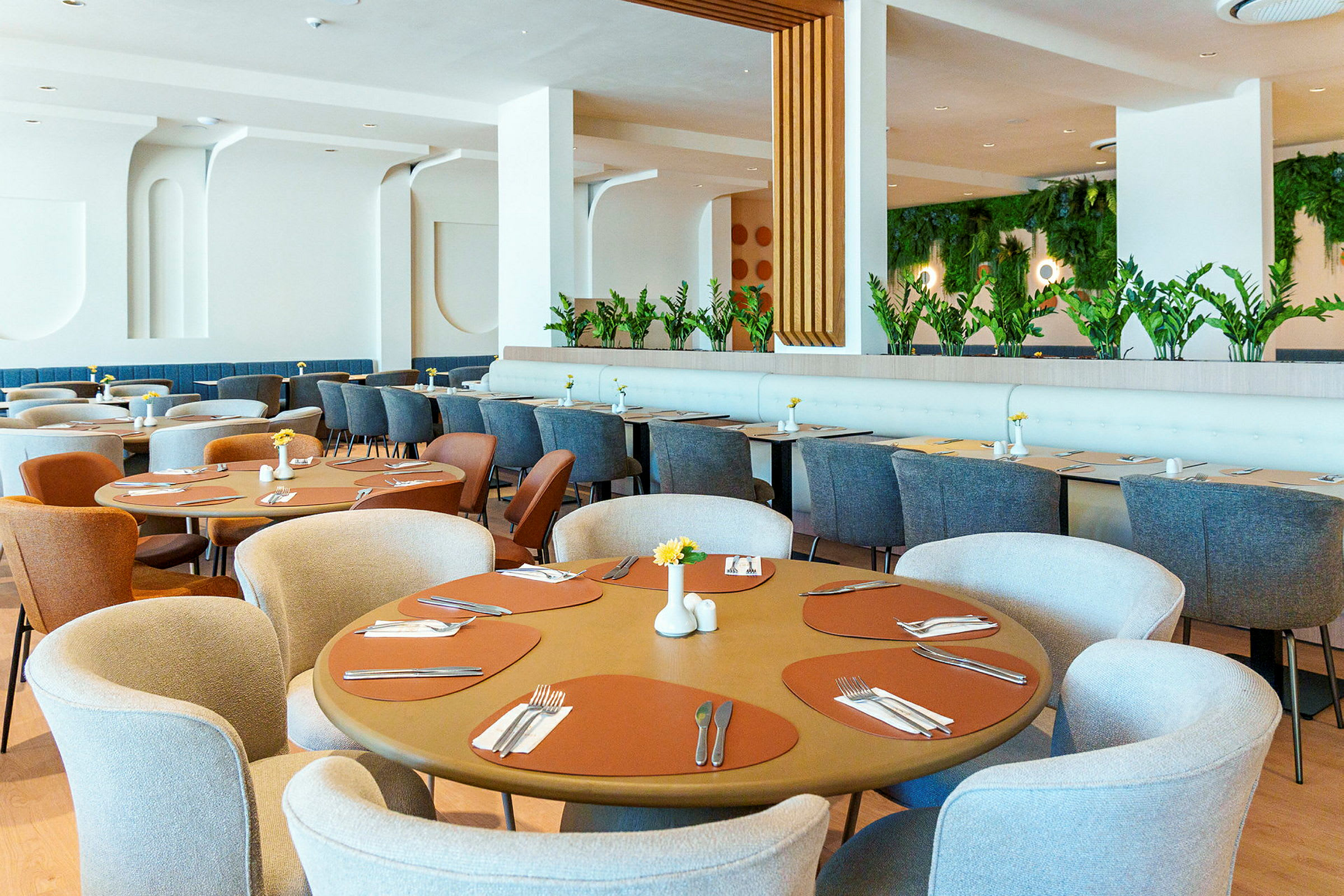 En restauranginteriör med runda och rektangulära bord, eleganta stolar och gröna växter som dekoration. (AI-genererad text)