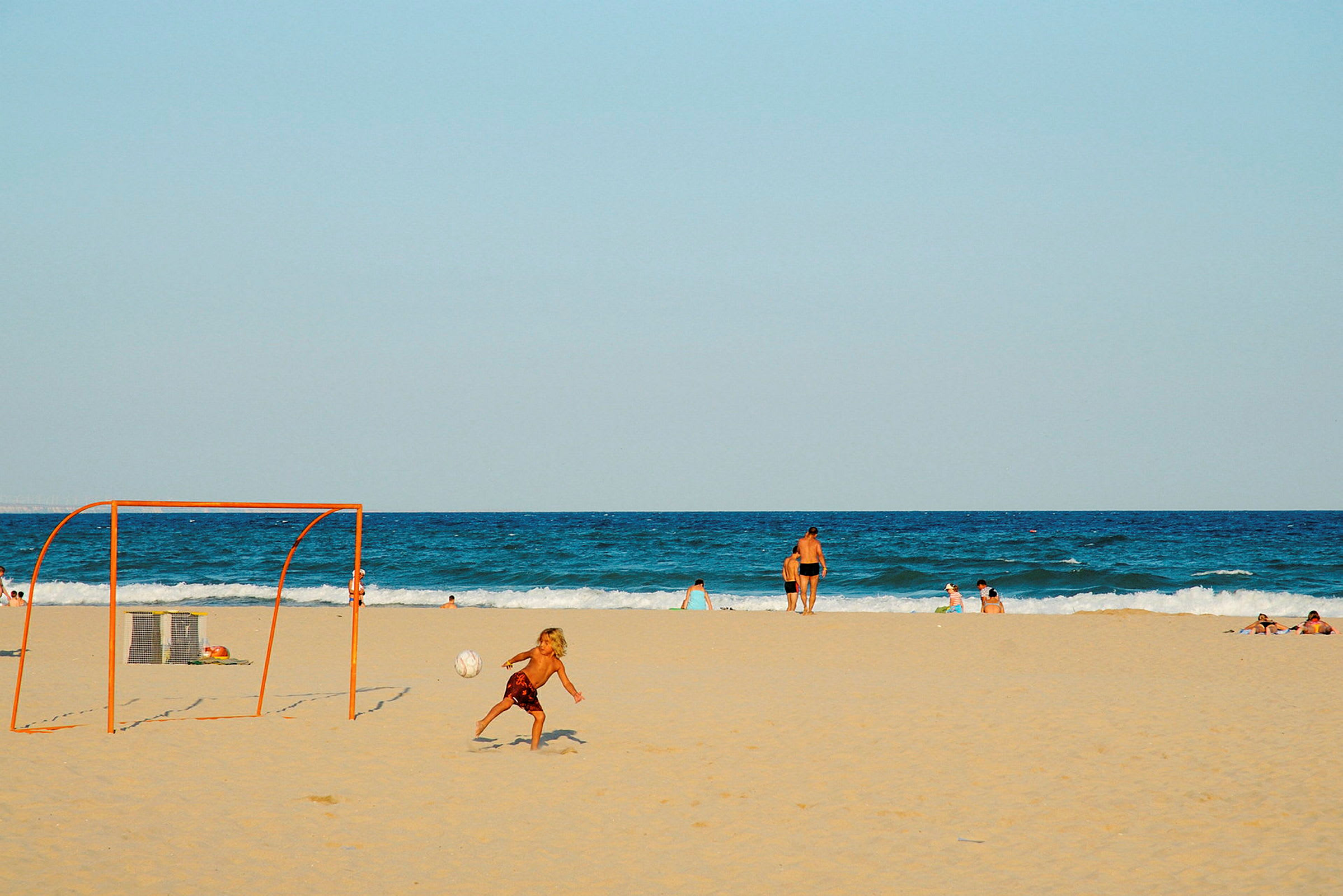 En strand med människor som simmar och en sandfotbollsmål. (AI-genererad text)