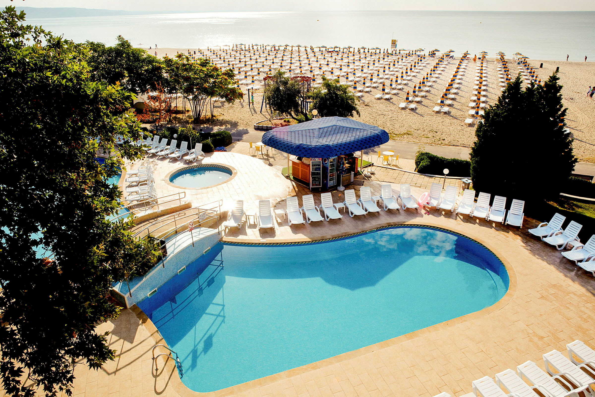 Poolområde med solstolar och en strand med solbäddar i bakgrunden. (AI-genererad text)