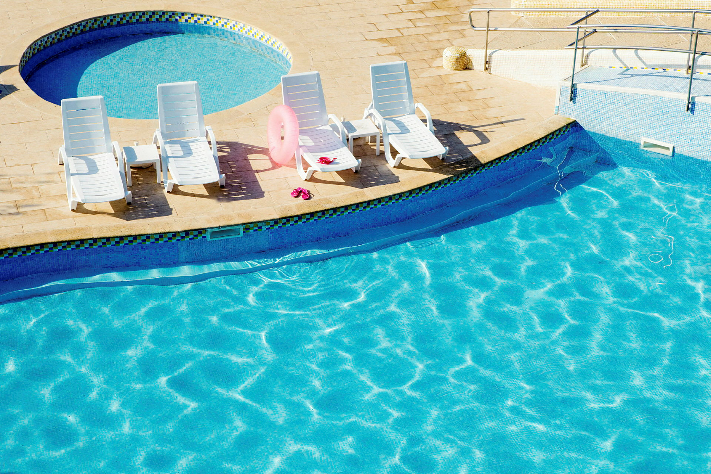 Fyra solstolar på en terrass vid en pool med klart vatten. (AI-genererad text)