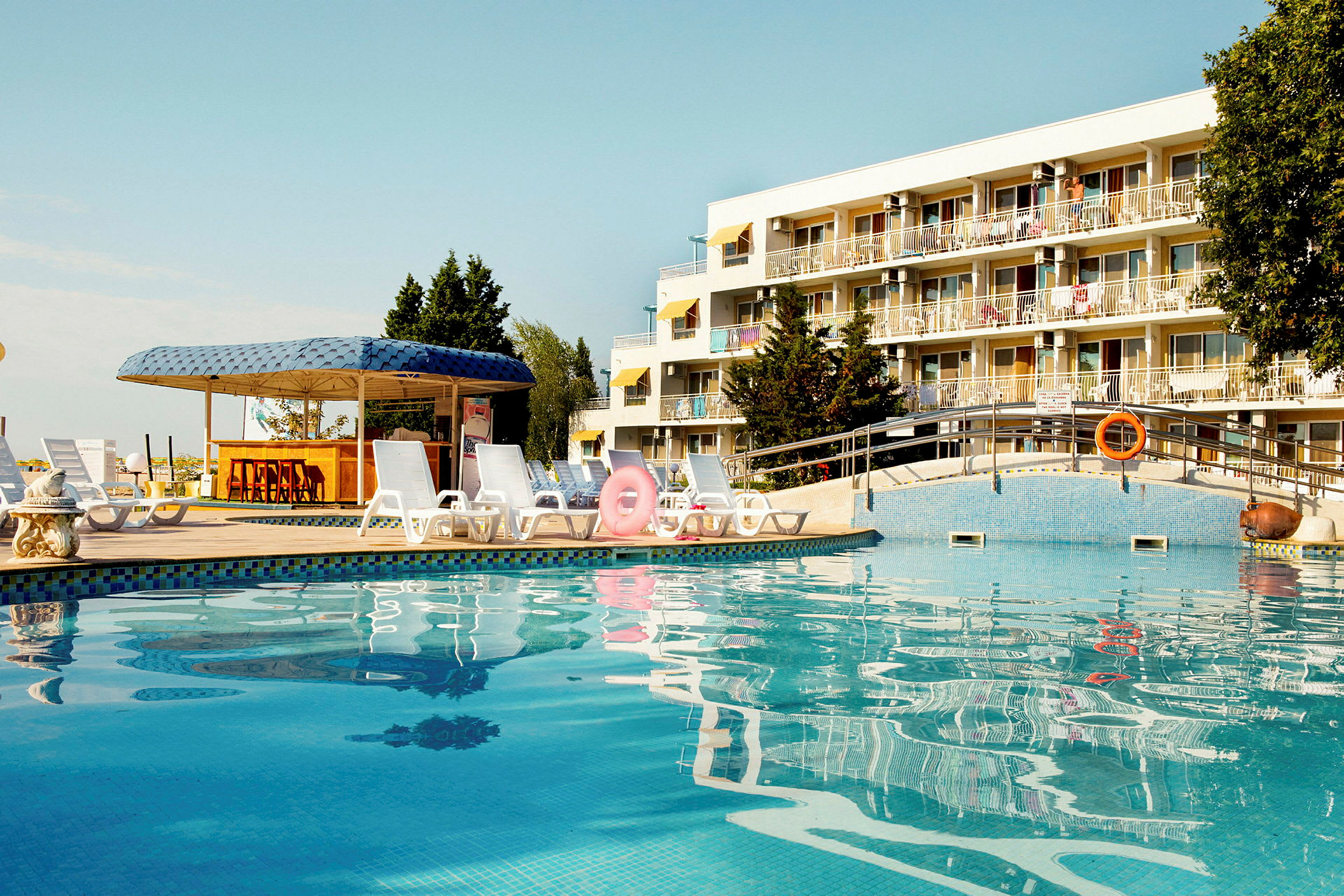 Utomhuspool med solstolar och parasoll framför ett hotell. (AI-genererad text)