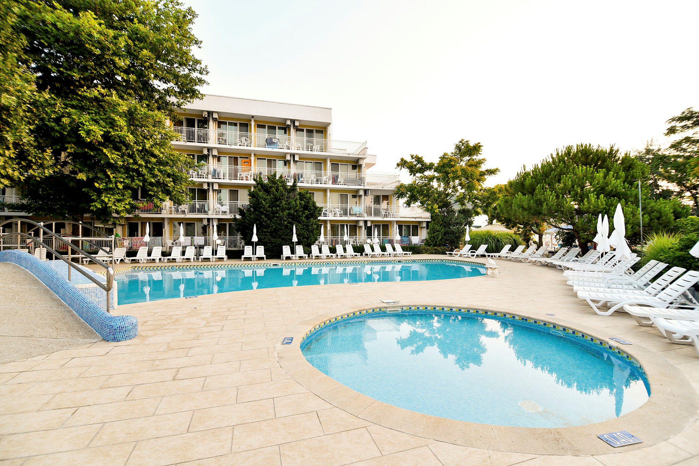 Hotellets poolområde med solstolar och omgivande grönska. (AI-genererad text)