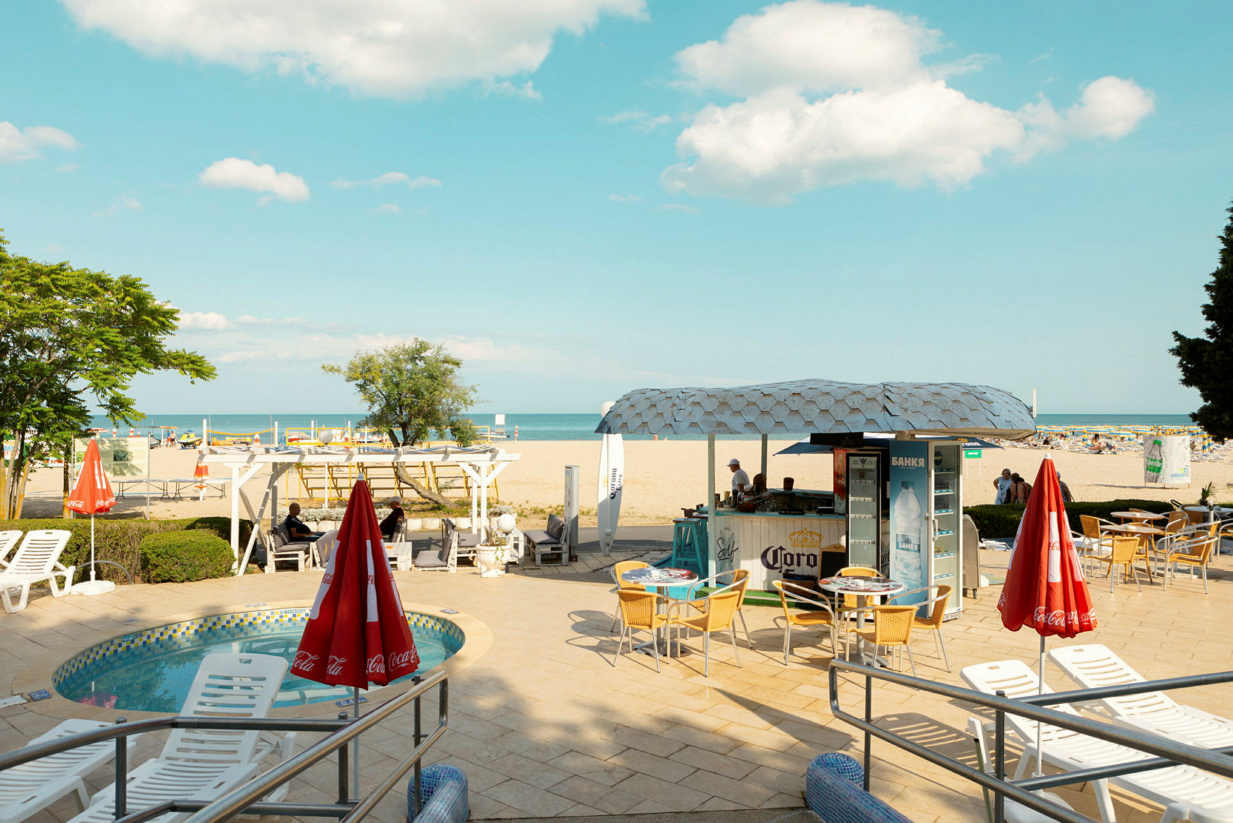 En strand med en kiosk och sittplatser framför, samt en liten pool. (AI-genererad text)