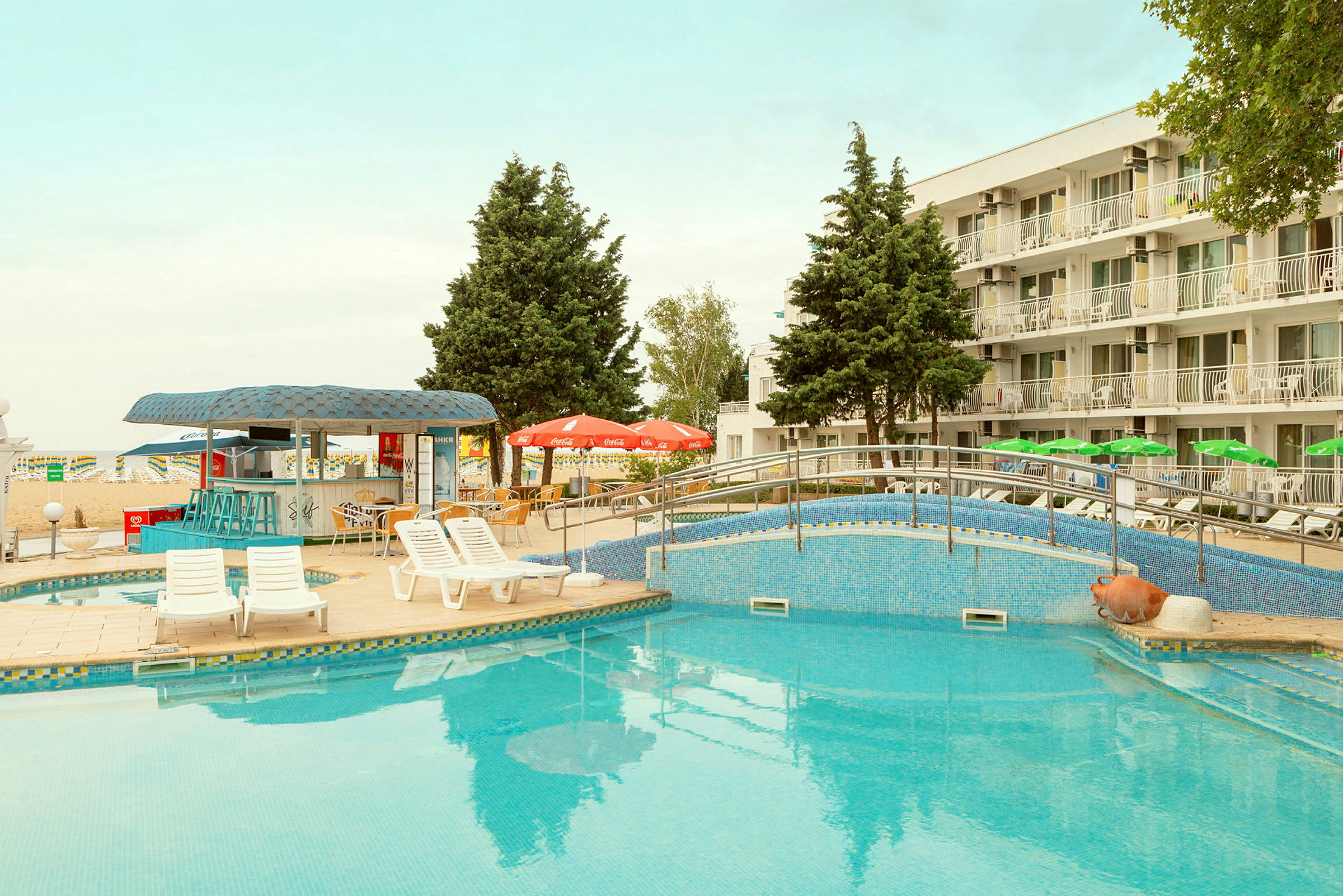En pool med solstolar och parasoll framför ett hotell. (AI-genererad text)