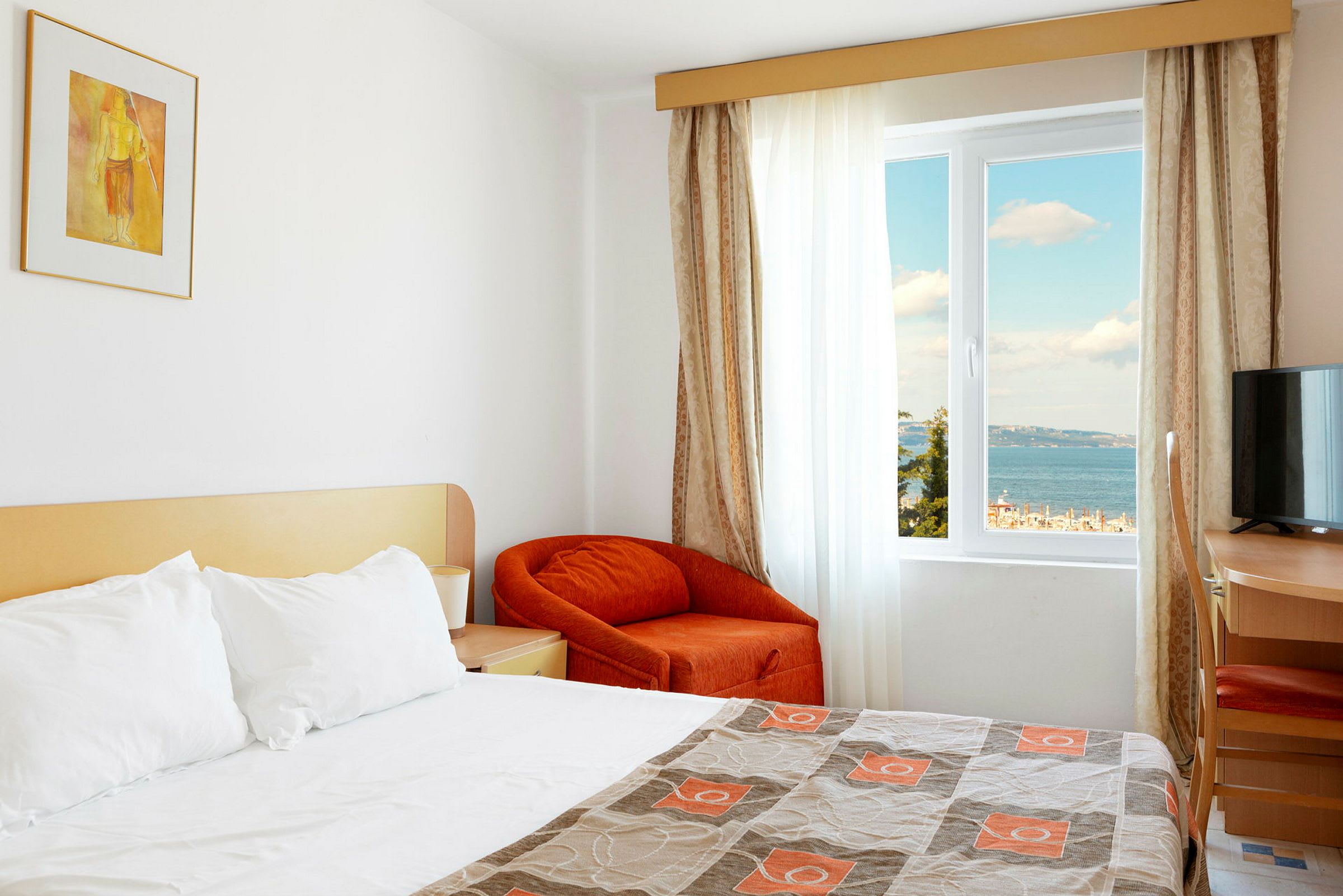 Hotellrum med en bäddad säng och utsikt över havet genom fönstret. (AI-genererad text)