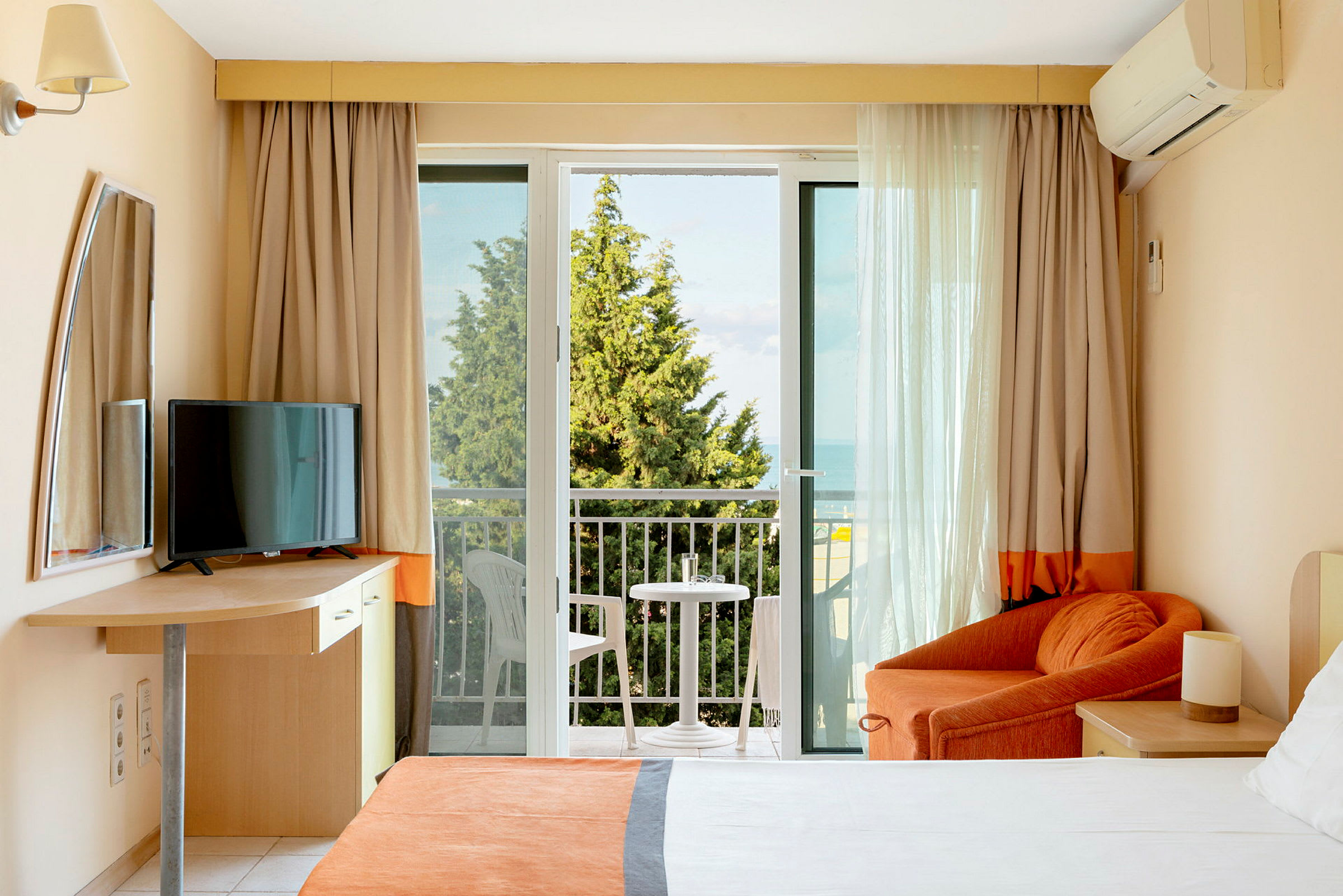 Ett hotellrum med balkong, säng, fåtölj och TV. (AI-genererad text)