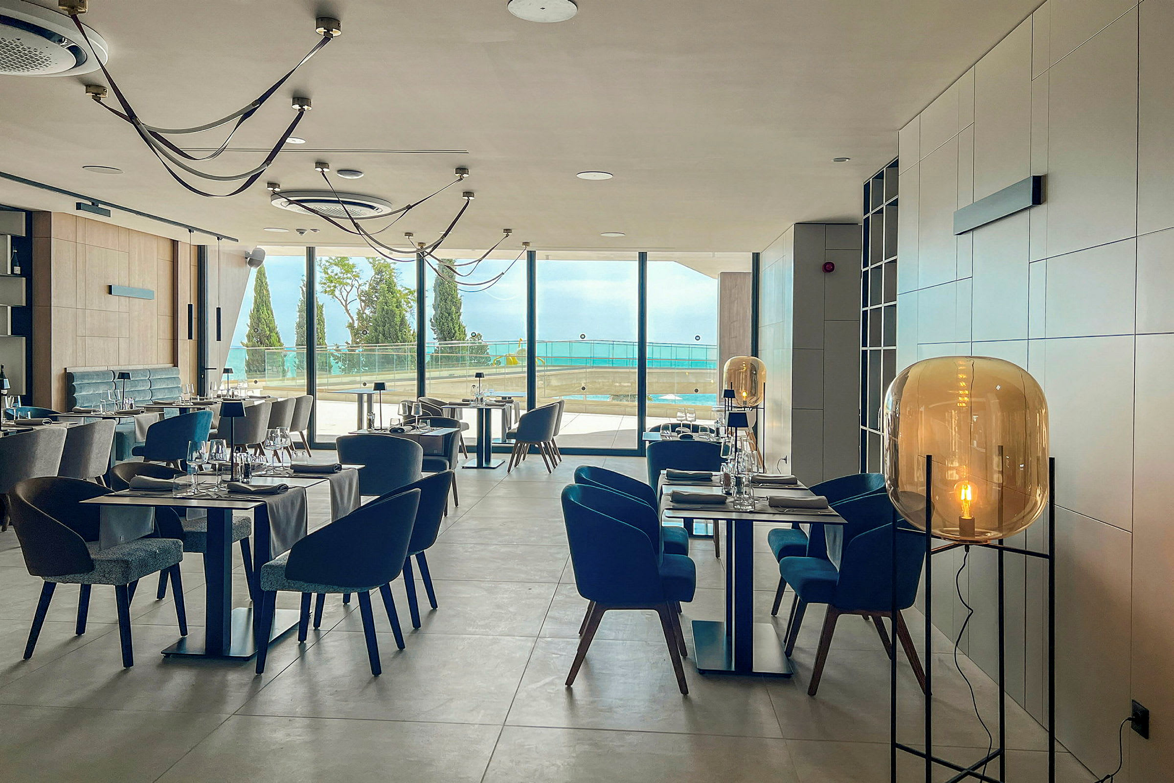 Restauranginteriör med modern design, uppställda bord och stolar och stora fönster med utsikt över havet. (AI-genererad text)