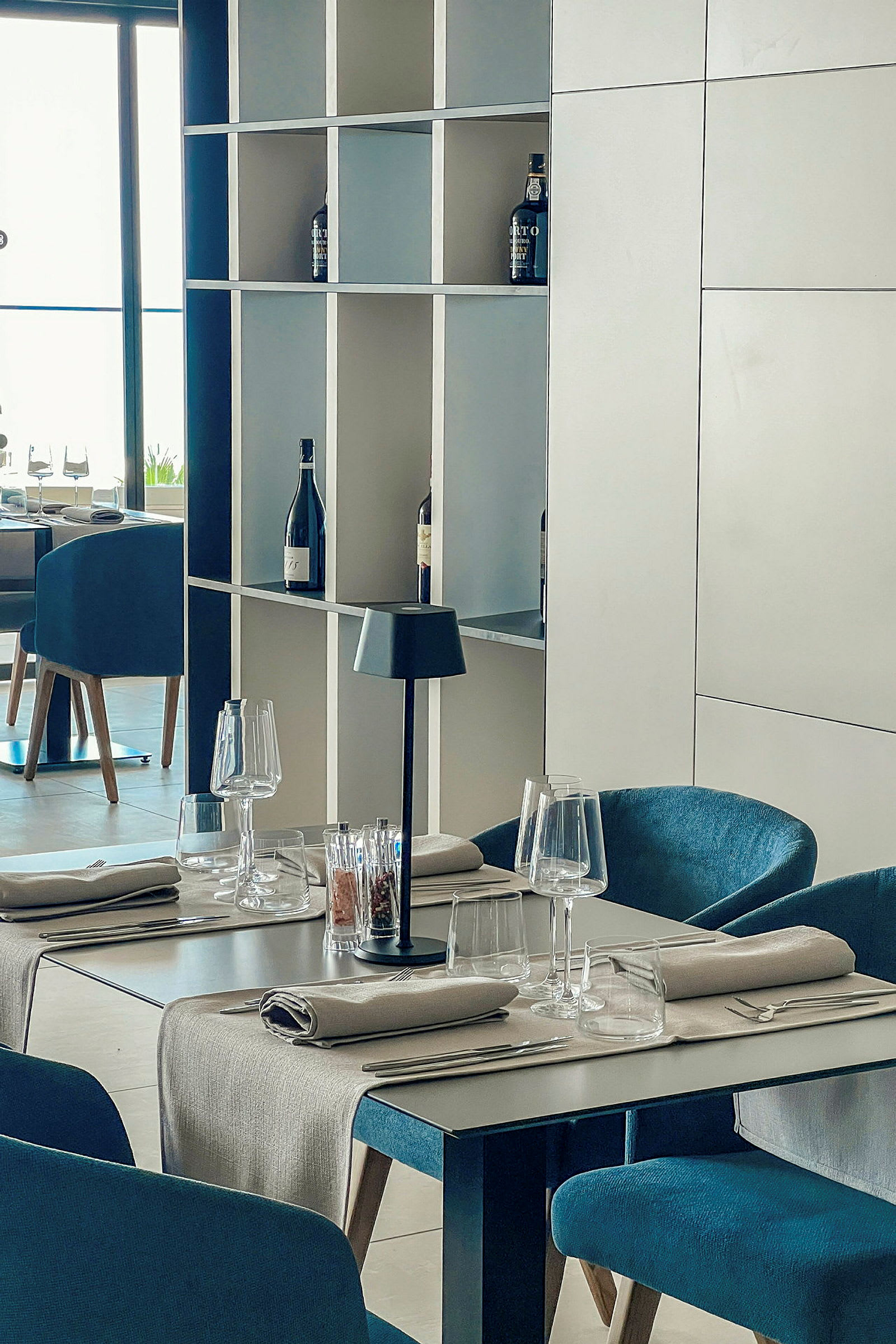 Restaurangbord med dukning samt hyllor med vinflaskor. (AI-genererad text)