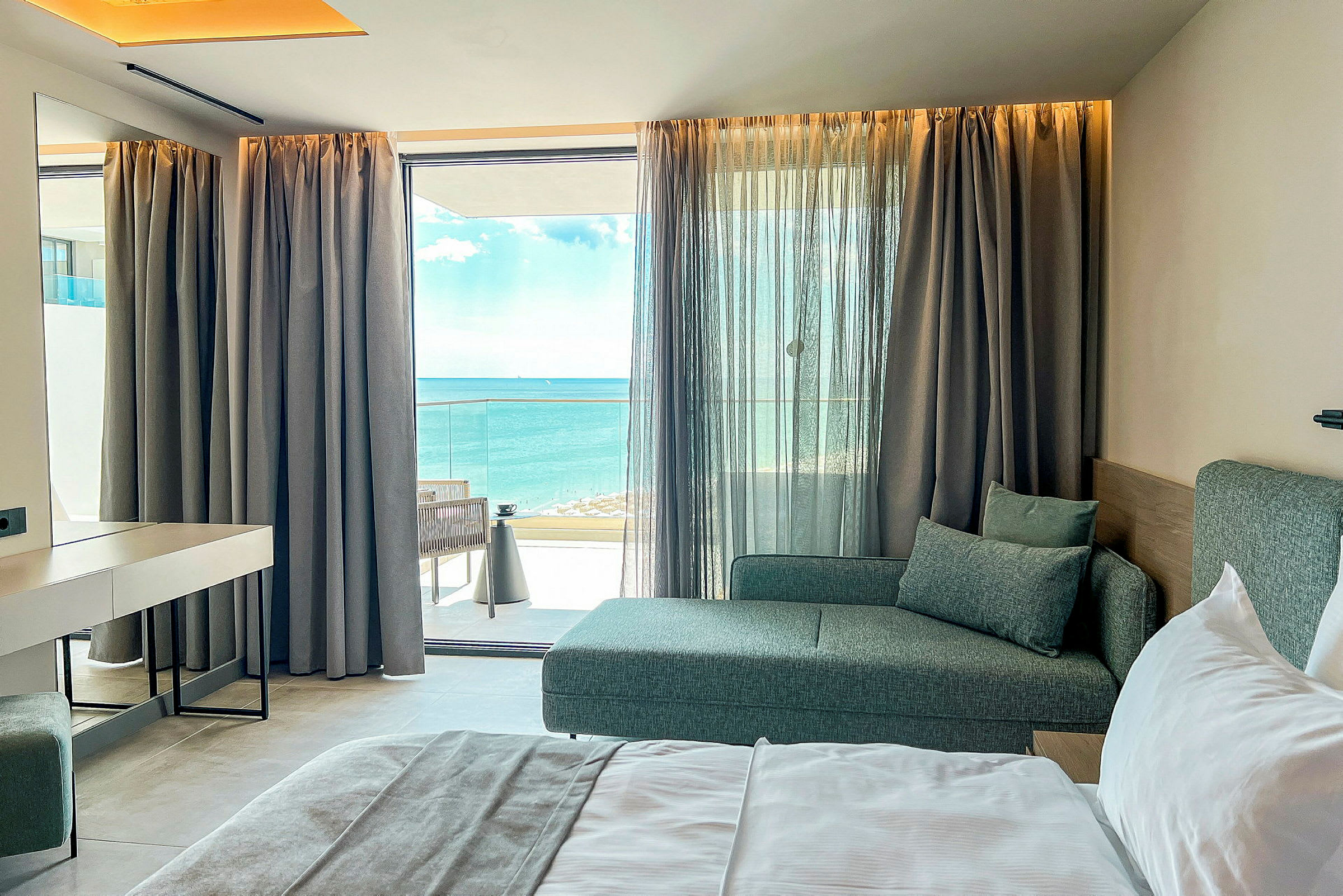 Hotelrum med säng, soffa och havsutsikt genom en fönsterfront. (AI-genererad text)