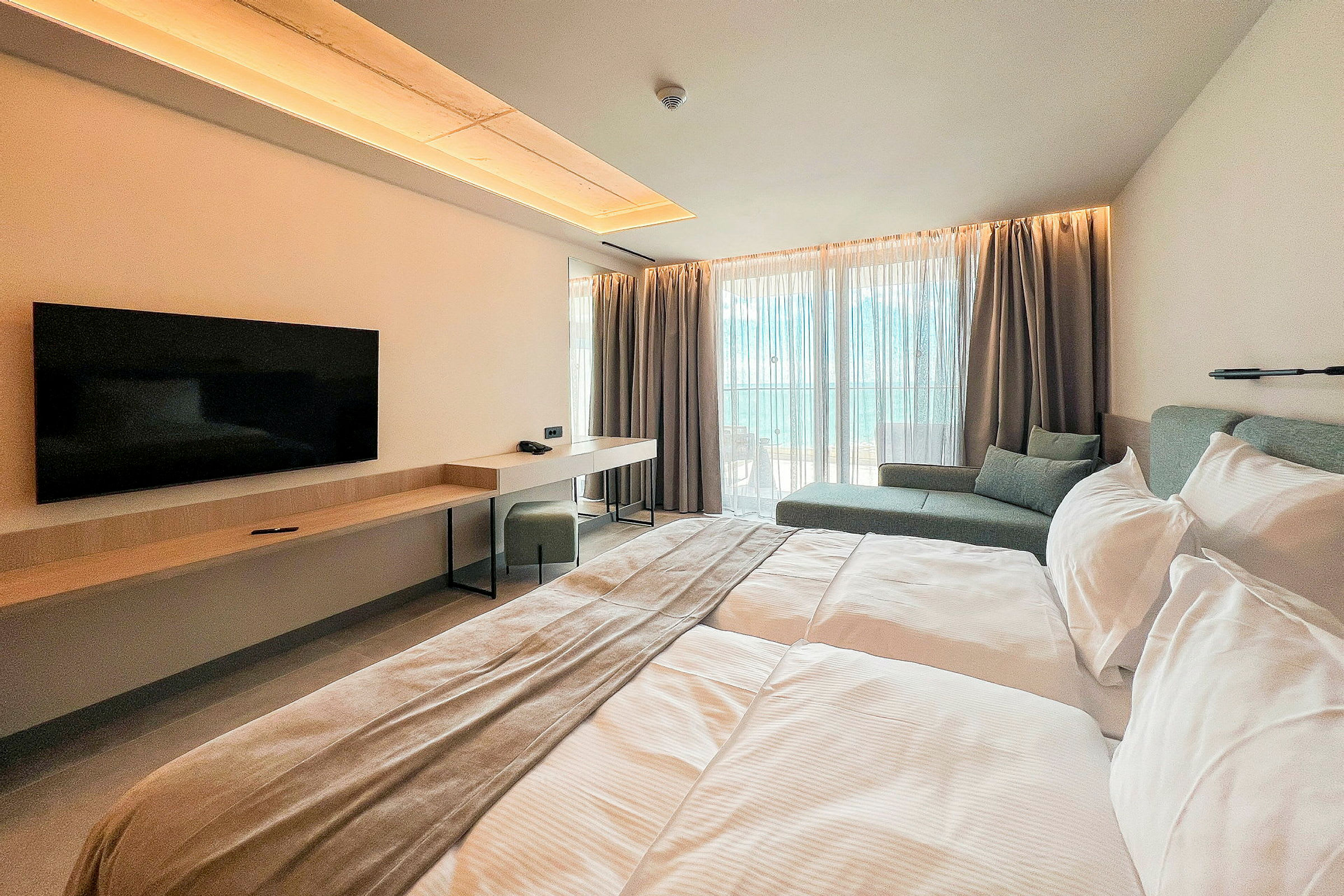 Ett modernt hotellrum med en dubbelsäng, en väggmonterad TV, skrivbord och sittområde vid stora fönster. (AI-genererad text)