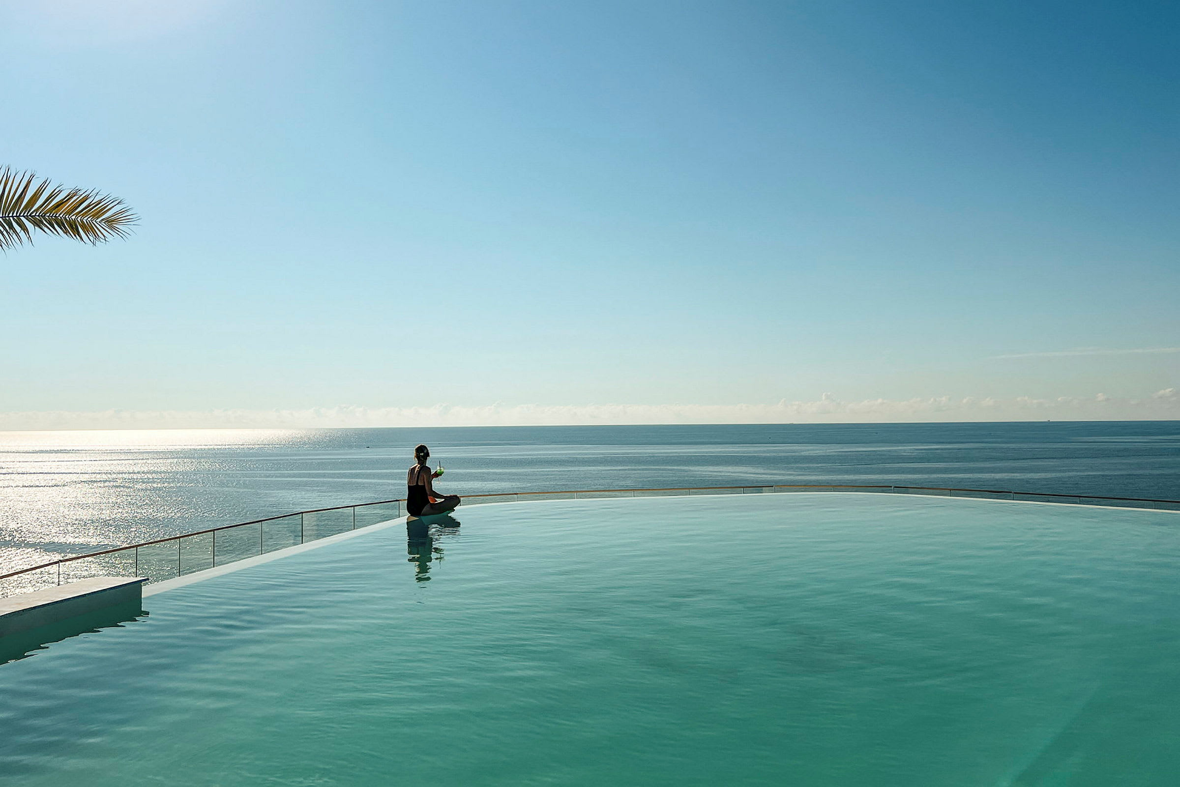 En person sitter vid kanten av en pool med havet i bakgrunden. (AI-genererad text)