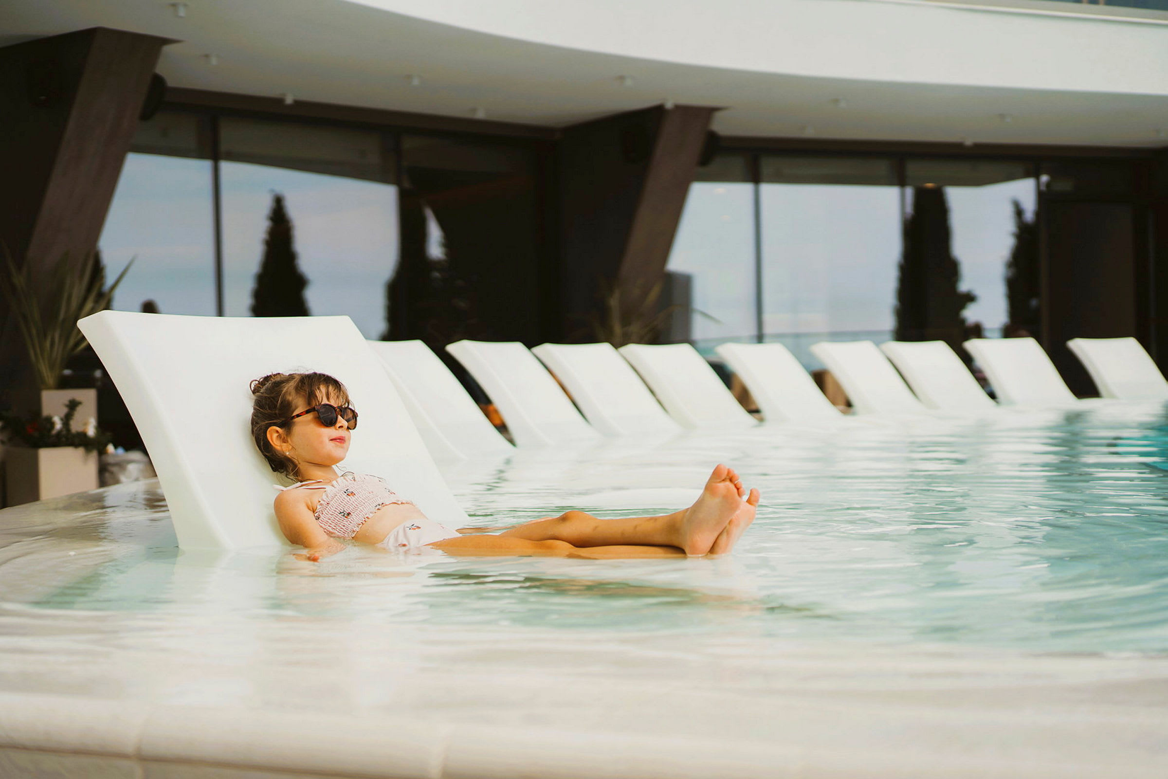 Ett barn ligger på en solstol i en pool vid ett modernt hotell. (AI-genererad text)