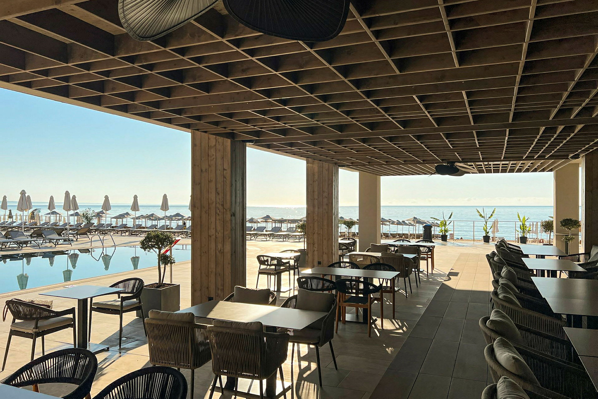 Restaurangområde under tak med utsikt över pool och hav. (AI-genererad text)