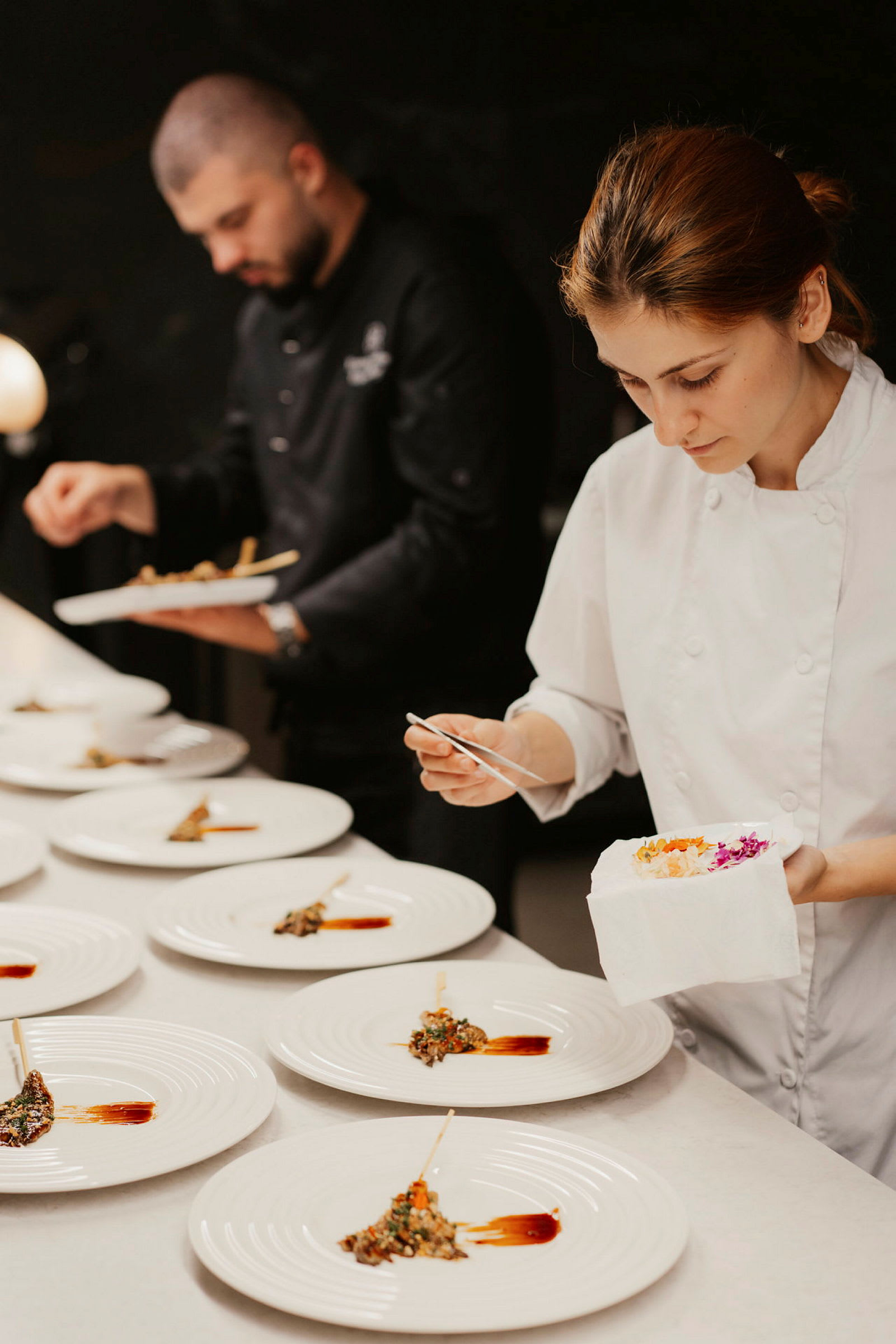Två personer i kökskläder förbereder tallrikar med gourmetmat. (AI-genererad text)