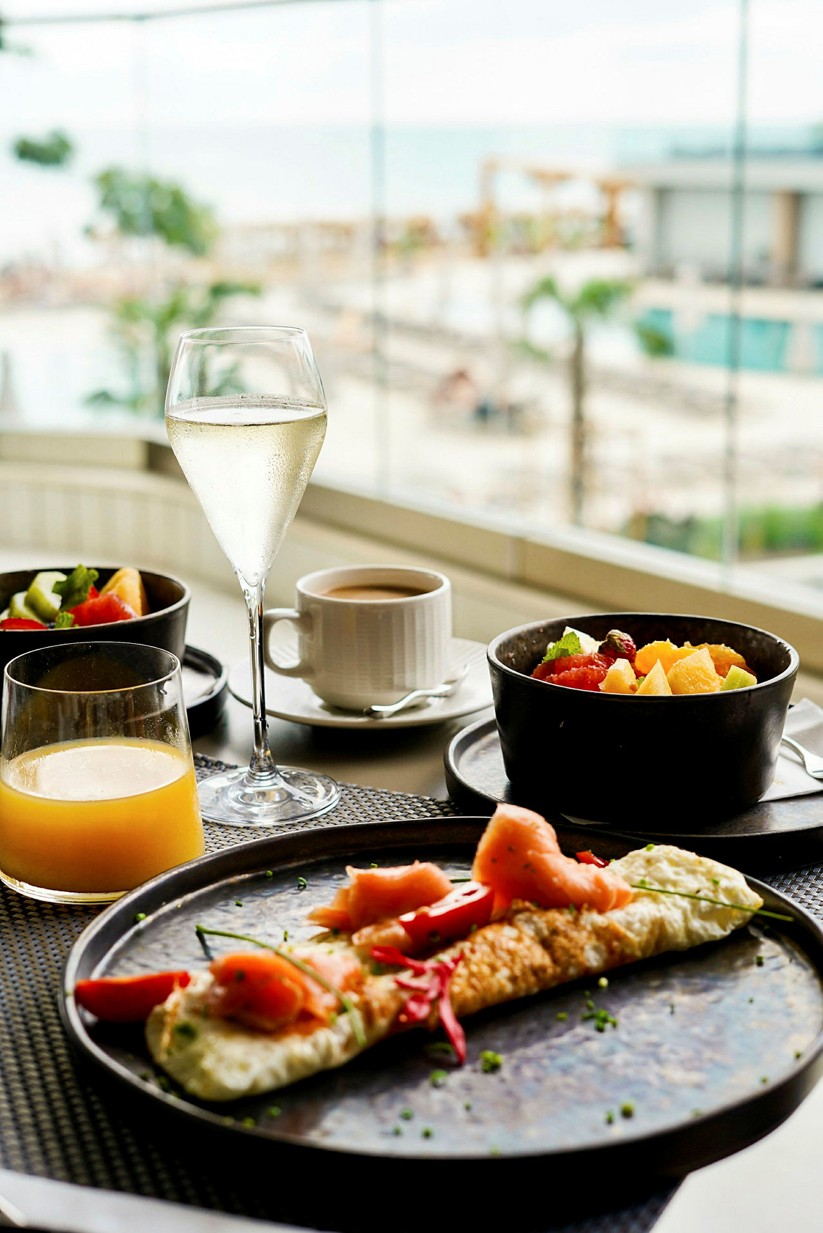 Frukost med en omelett, färska frukter och drycker, med utsikt mot en pool och havet. (AI-genererad text)
