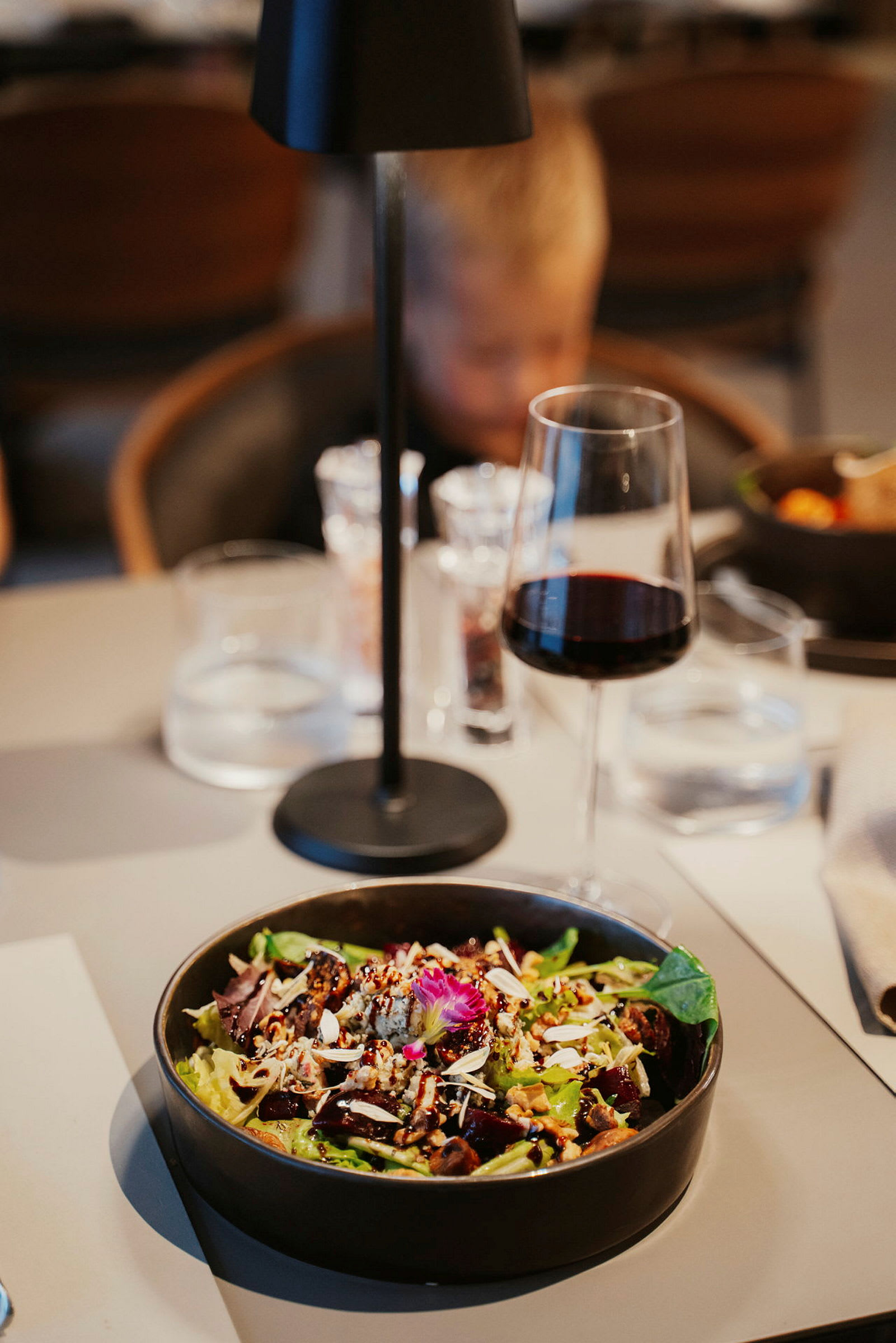 En skål med sallad prydd med nötter och blommor på ett dukat bord. (AI-genererad text)