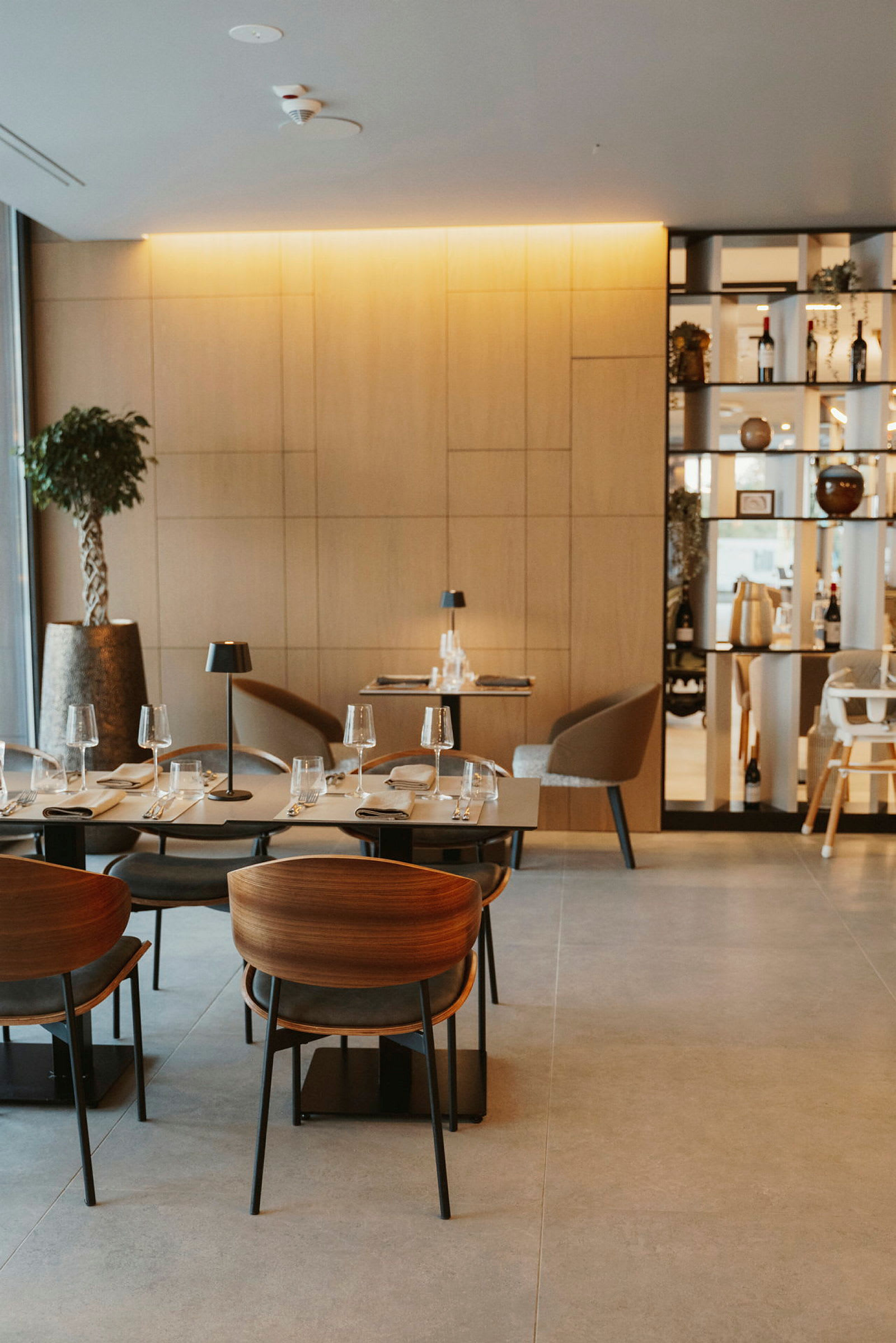 En modern restaurang med träpaneler, eleganta bord och stolar, samt glas och tallrikar uppställda för servering. (AI-genererad text)