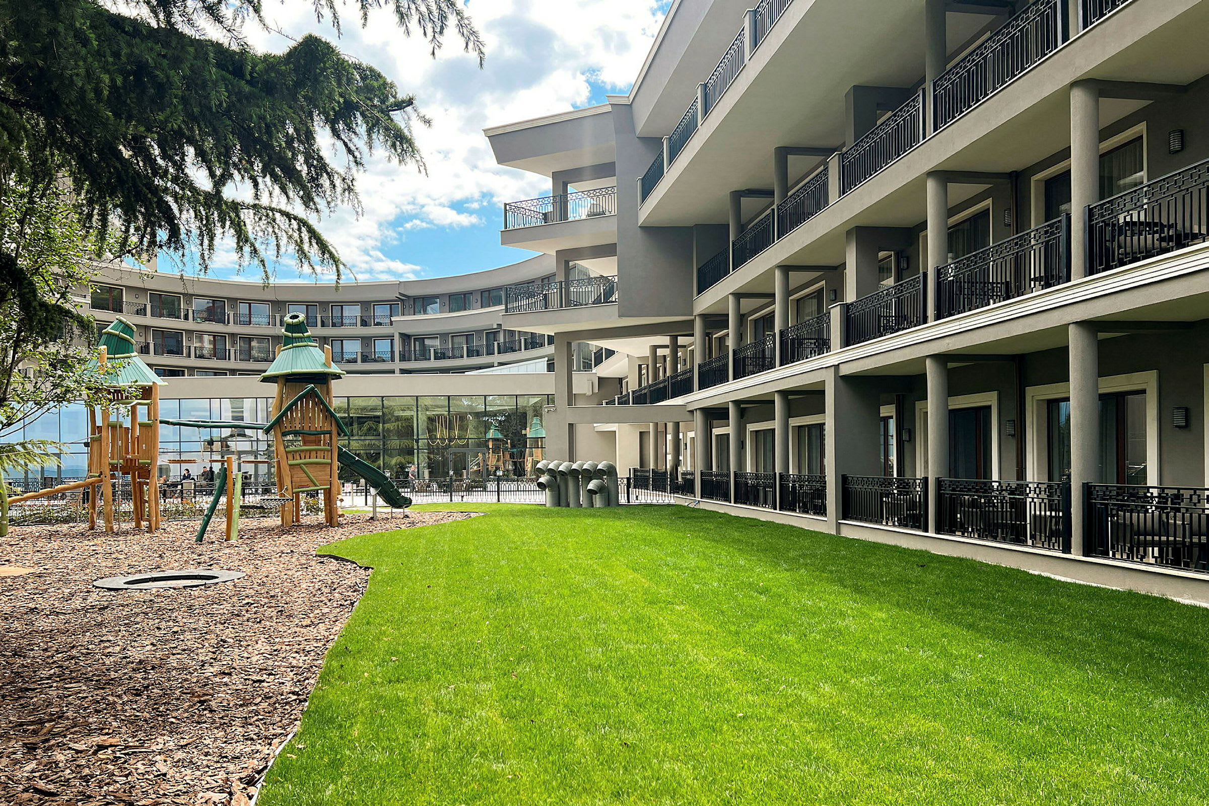 Hotellbyggnad vid grön gräsmatta och lekplats. (AI-genererad text)