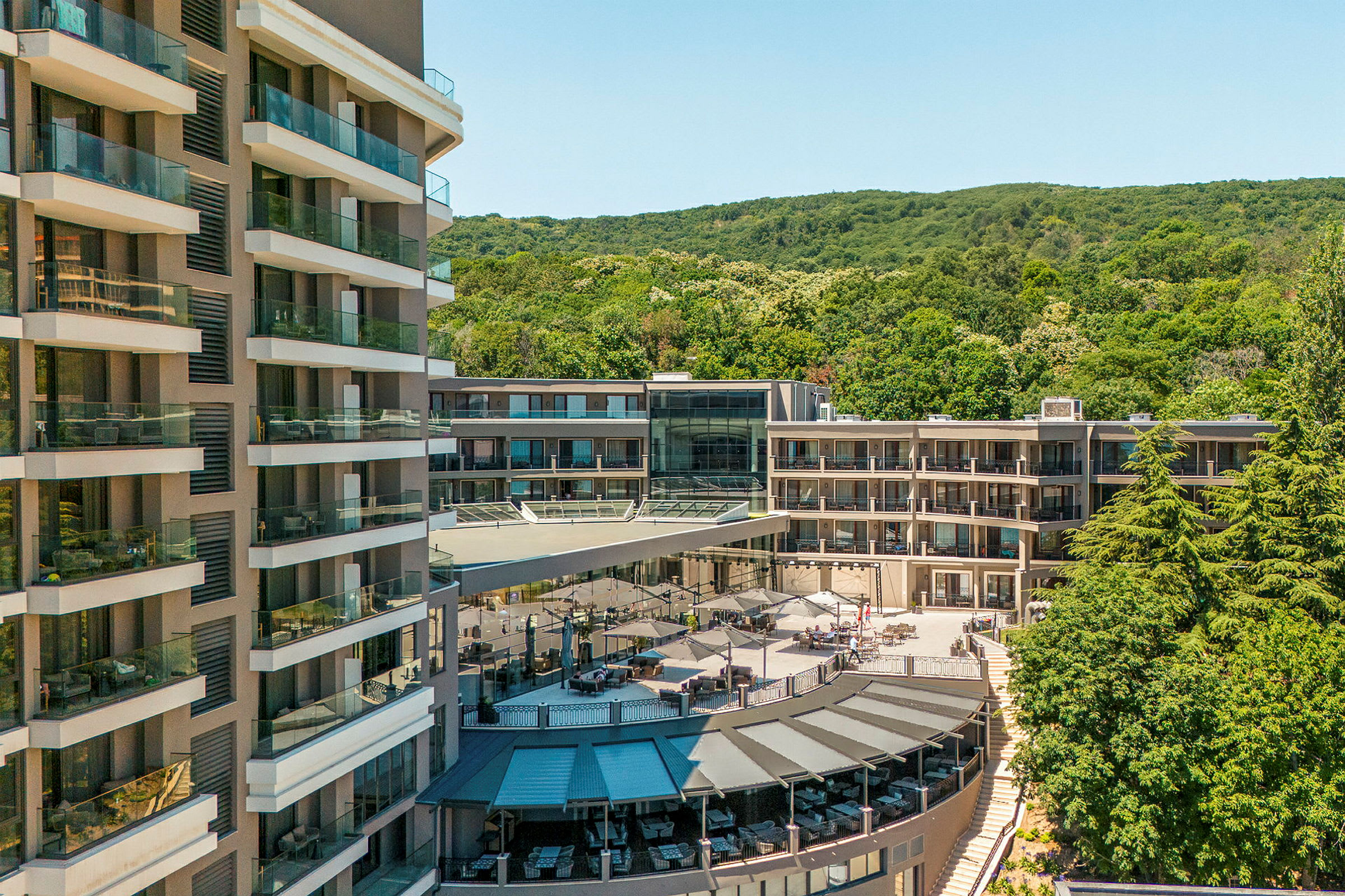 Flera hotellbyggnader omgivna av grönska och en terrass med parasoller. (AI-genererad text)