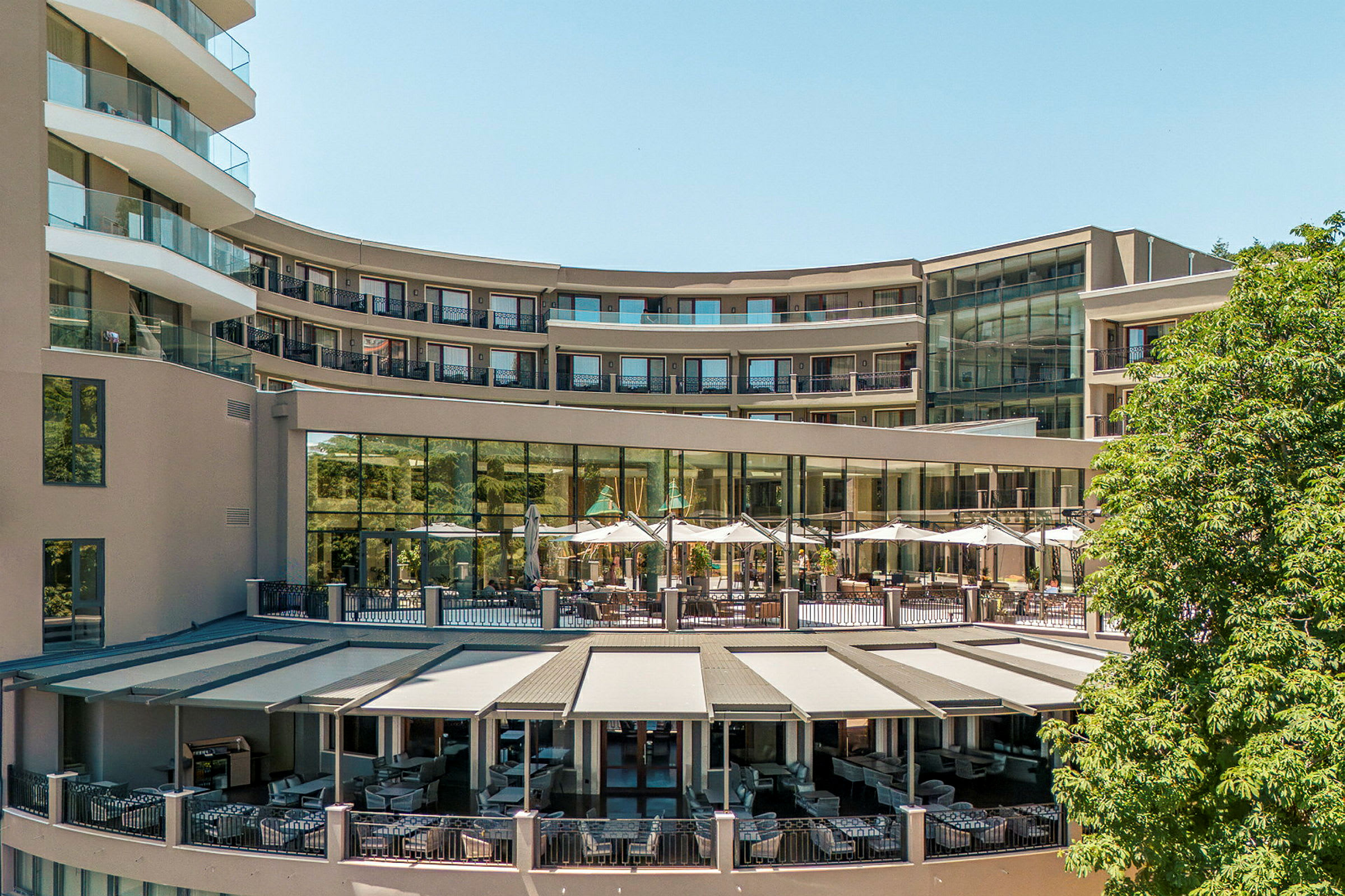 Hotellbyggnad med utomhusterrass och solskydd. (AI-genererad text)