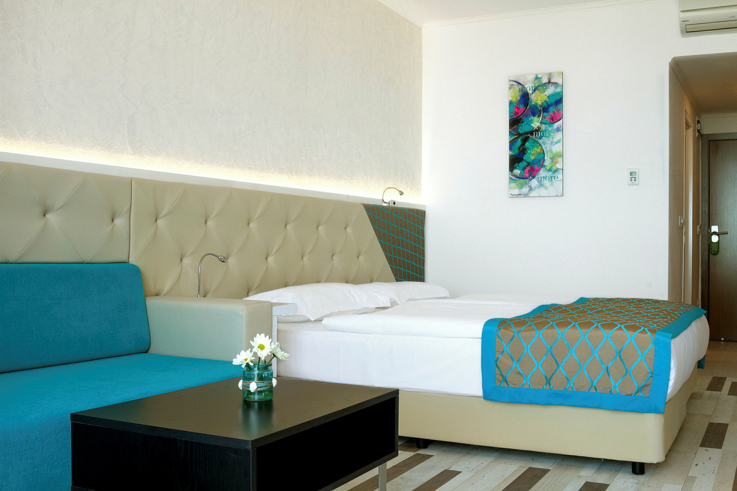 Ett modernt hotellrum med en dubbelsäng, turkos soffa och väggkonst. (AI-genererad text)