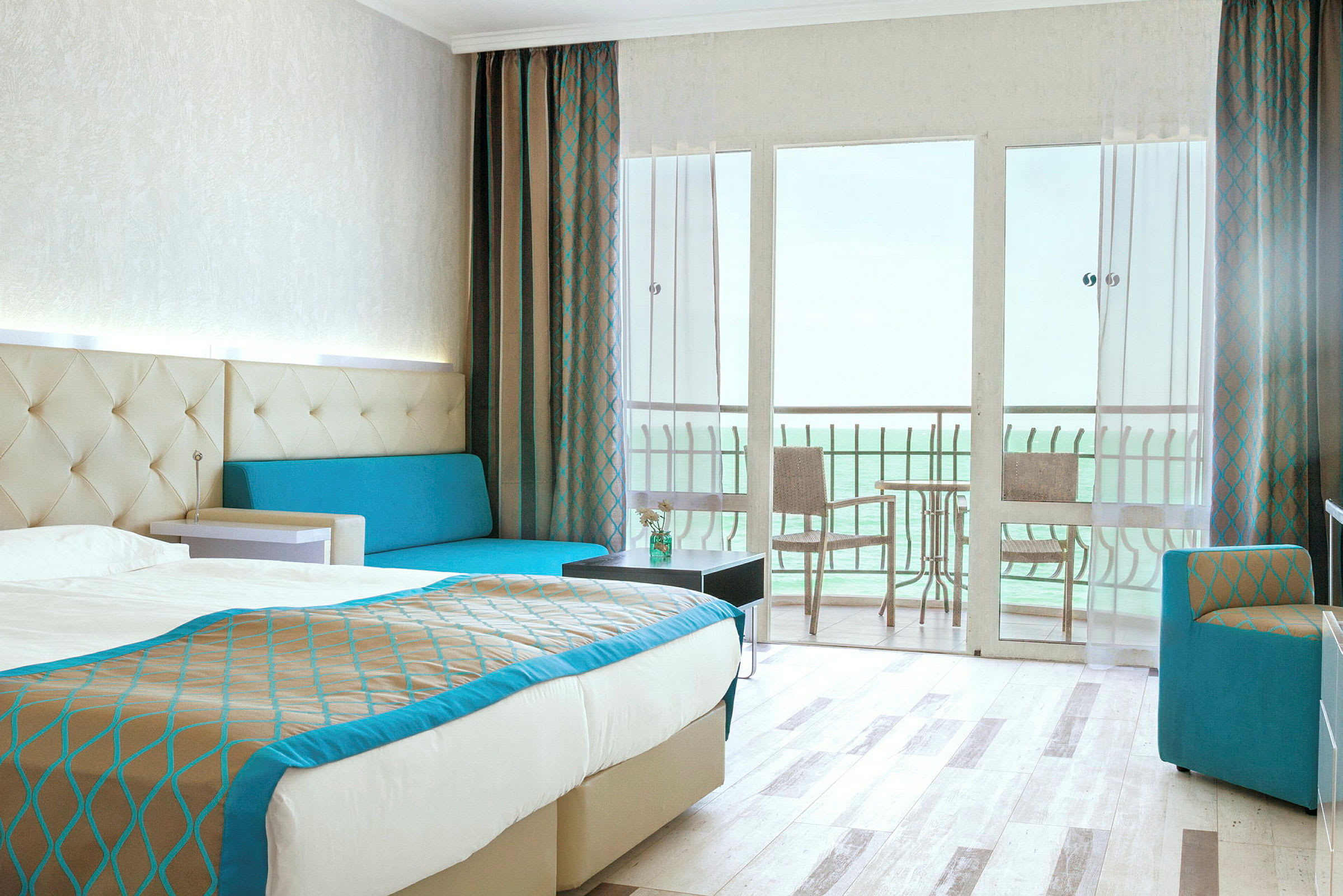 Hotellrum med dubbelsäng, soffa, och balkong med utsikt över havet. (AI-genererad text)