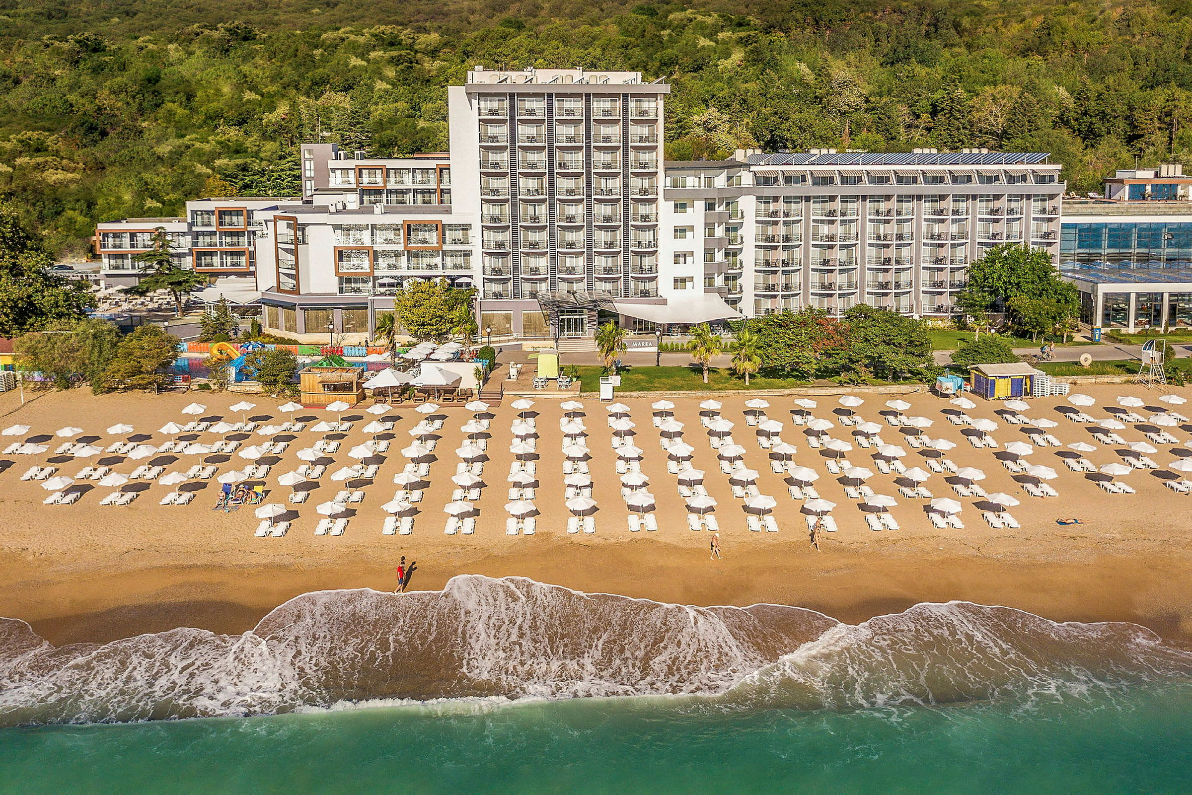 Strand med uppställda solstolar och parasoller framför ett hotell. (AI-genererad text)
