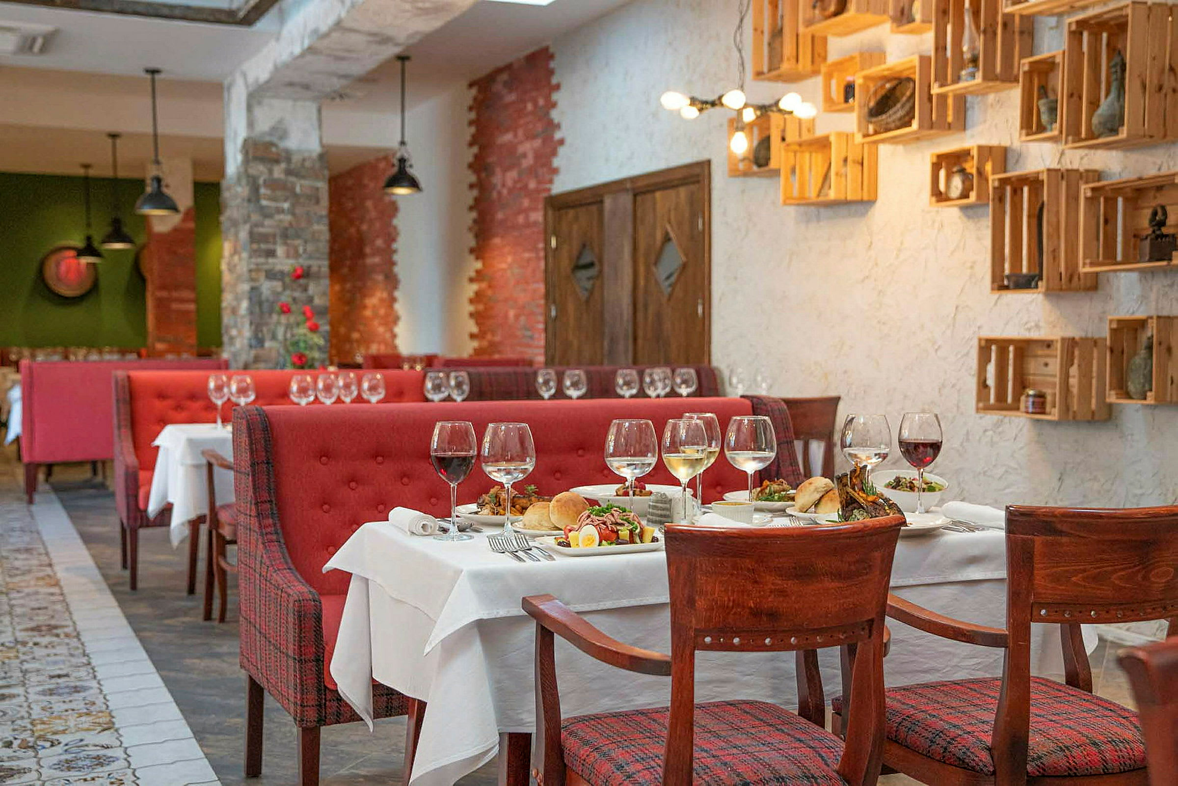 En restaurang med röda soffor, trästolar och dukade bord med vinglas och matupplägg. (AI-genererad text)
